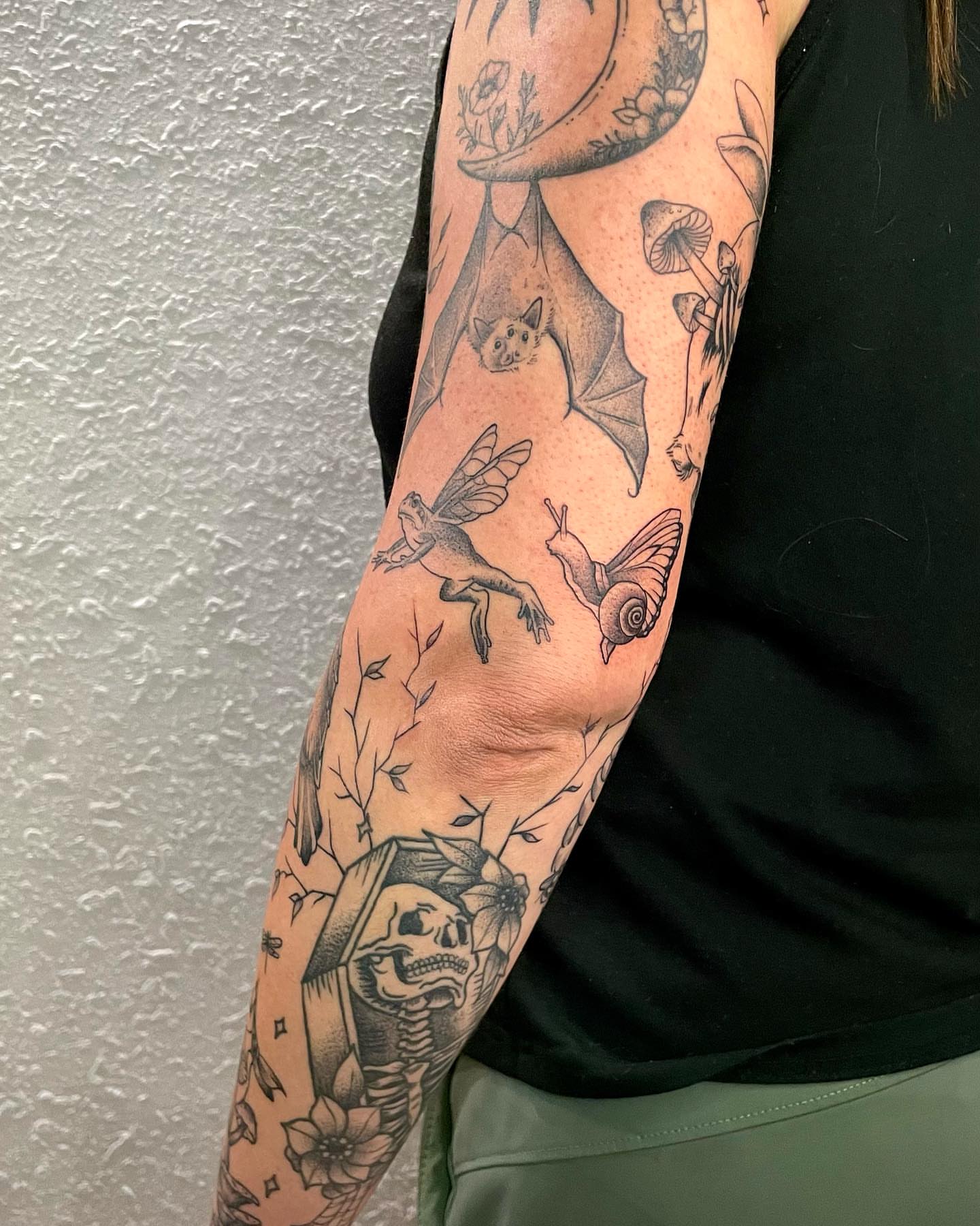Bat, fairy, snail, skull, flowers black and grey tattoo on the forearm by Bryce Presley, Mission, Kansas
