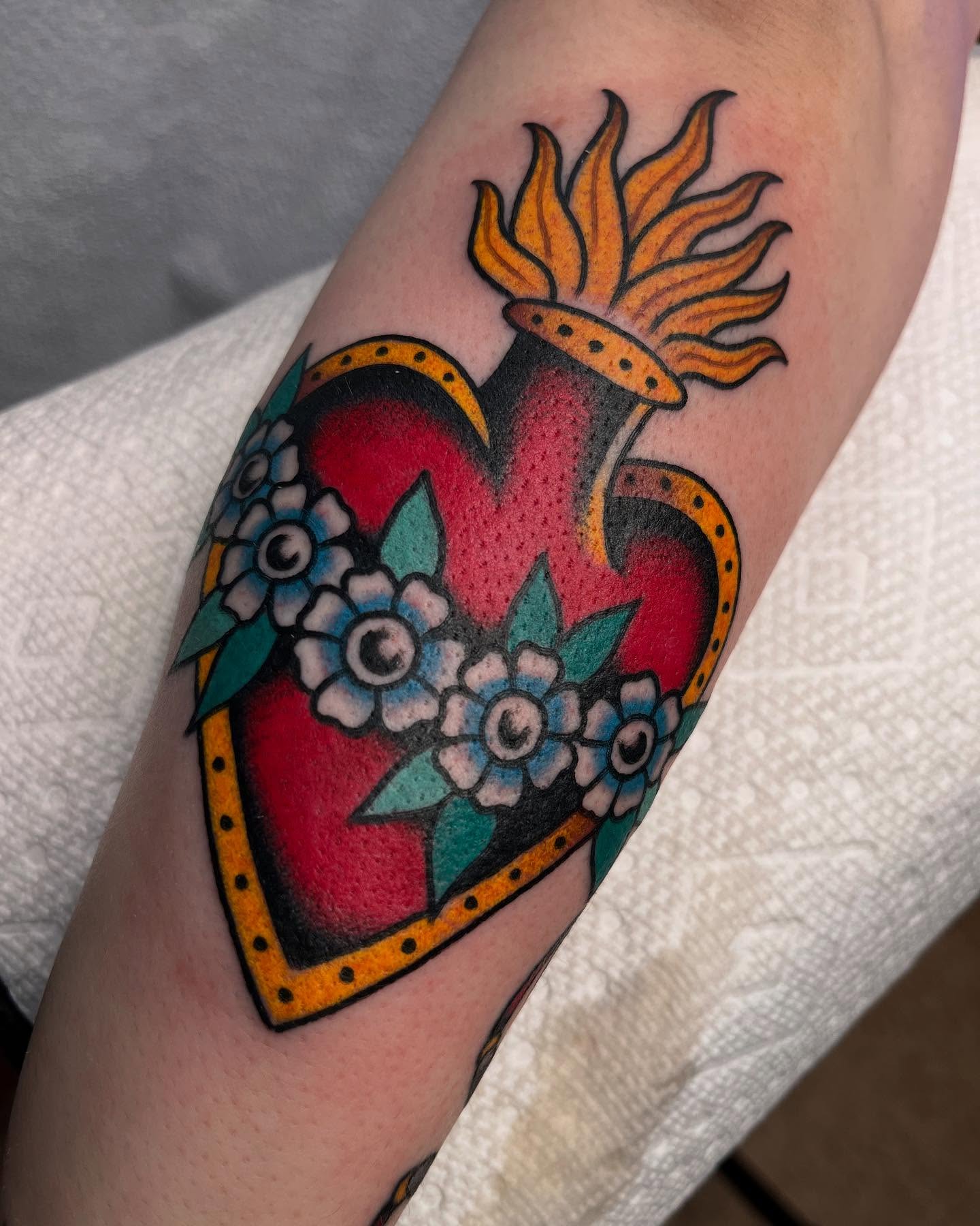 Heart with flames American traditional tattoo on the forearm by ๐๐ฎ๐ฌ๐ญ๐ข๐ง ๐๐จ๐ฐ๐๐ซ๐, Oakland, California