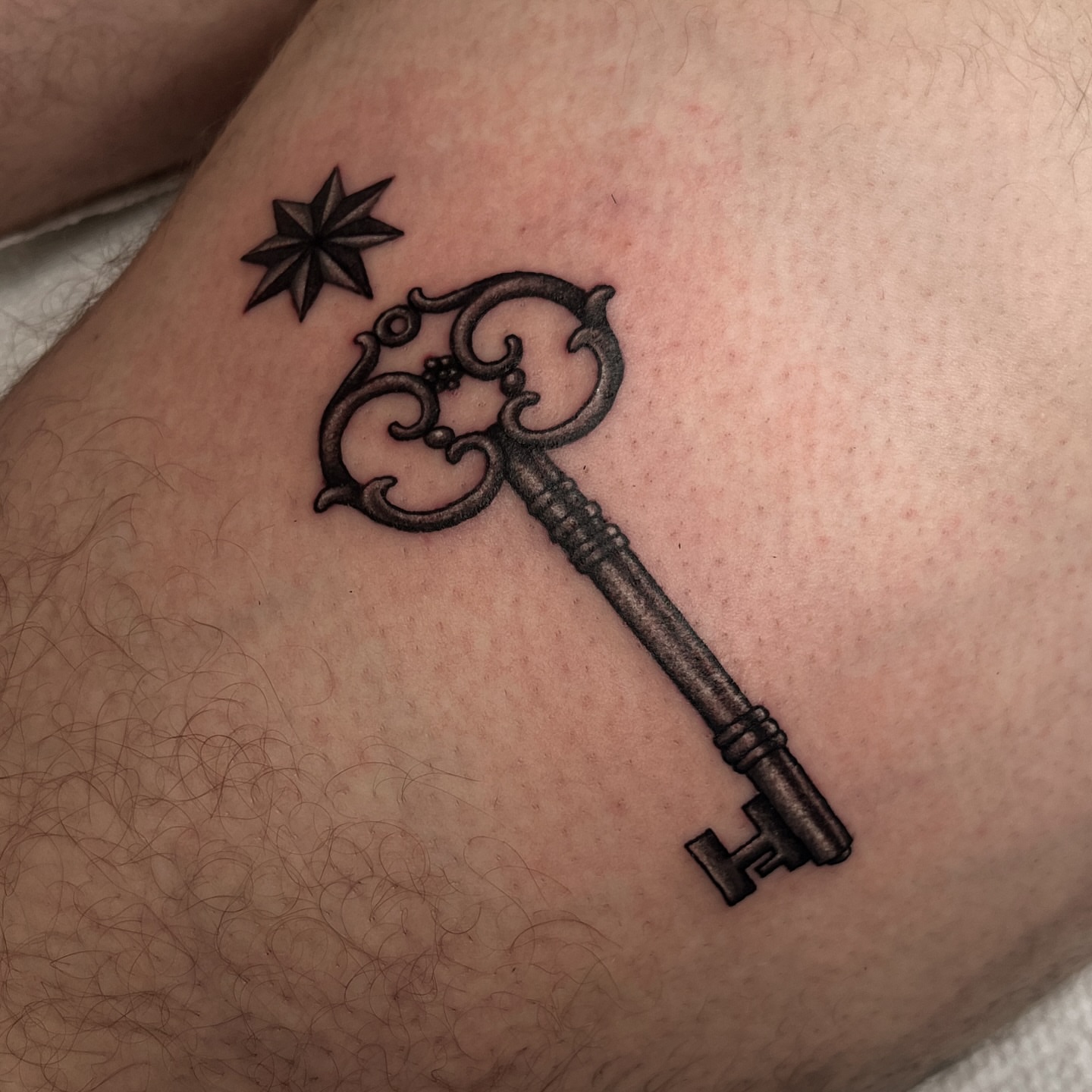 Key and star black and grey tattoo on the thigh by Téa Fish