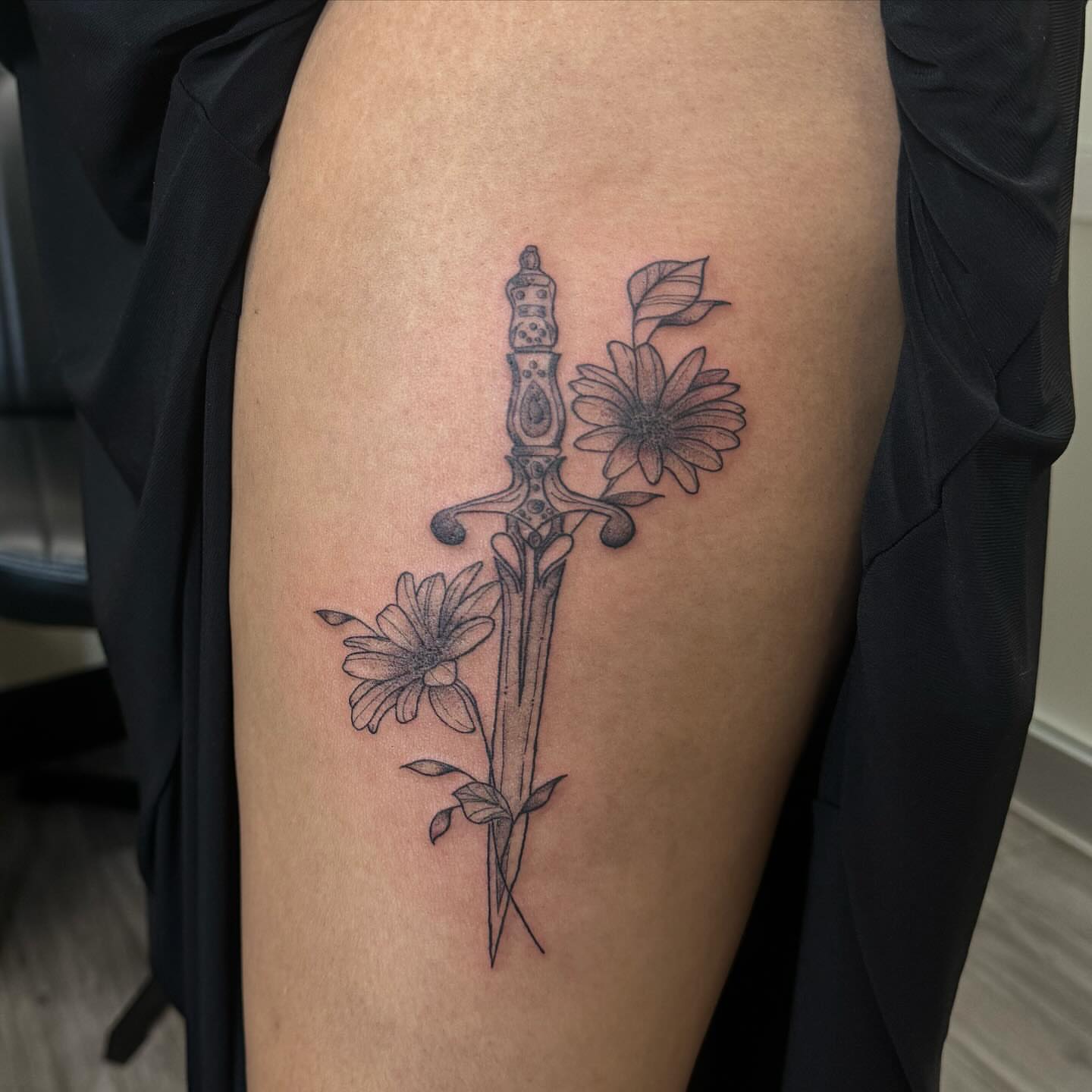 Sword and flowers black and grey tattoo on the thigh by Gladys L.