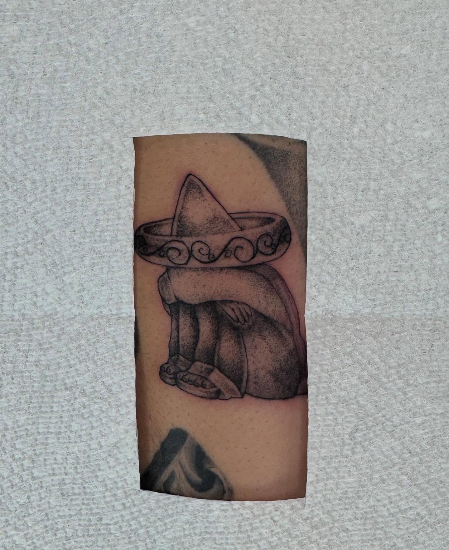 Sombrero-wearing figure black and grey tattoo on the forearm by Alexa Camacho