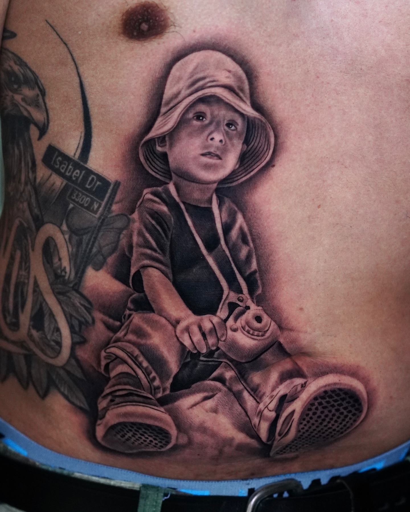 Child with toy gun realism tattoo on the torso by Luis Peña