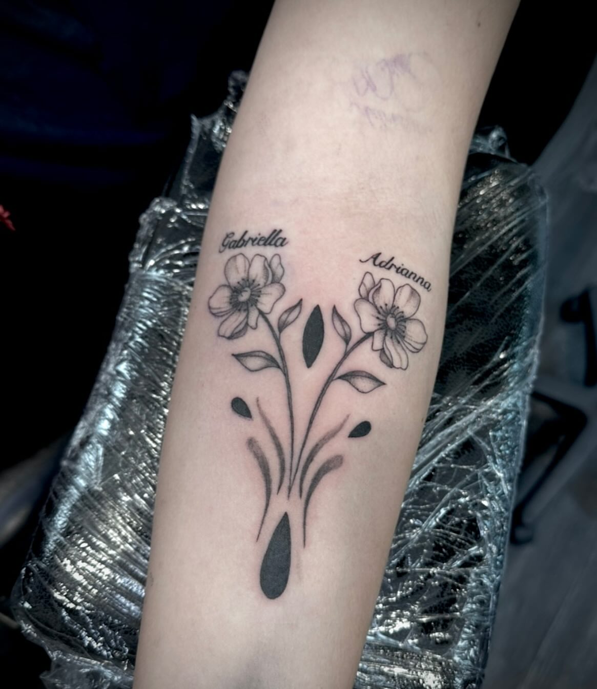 Flowers and names black and grey tattoo on the forearm by Bell