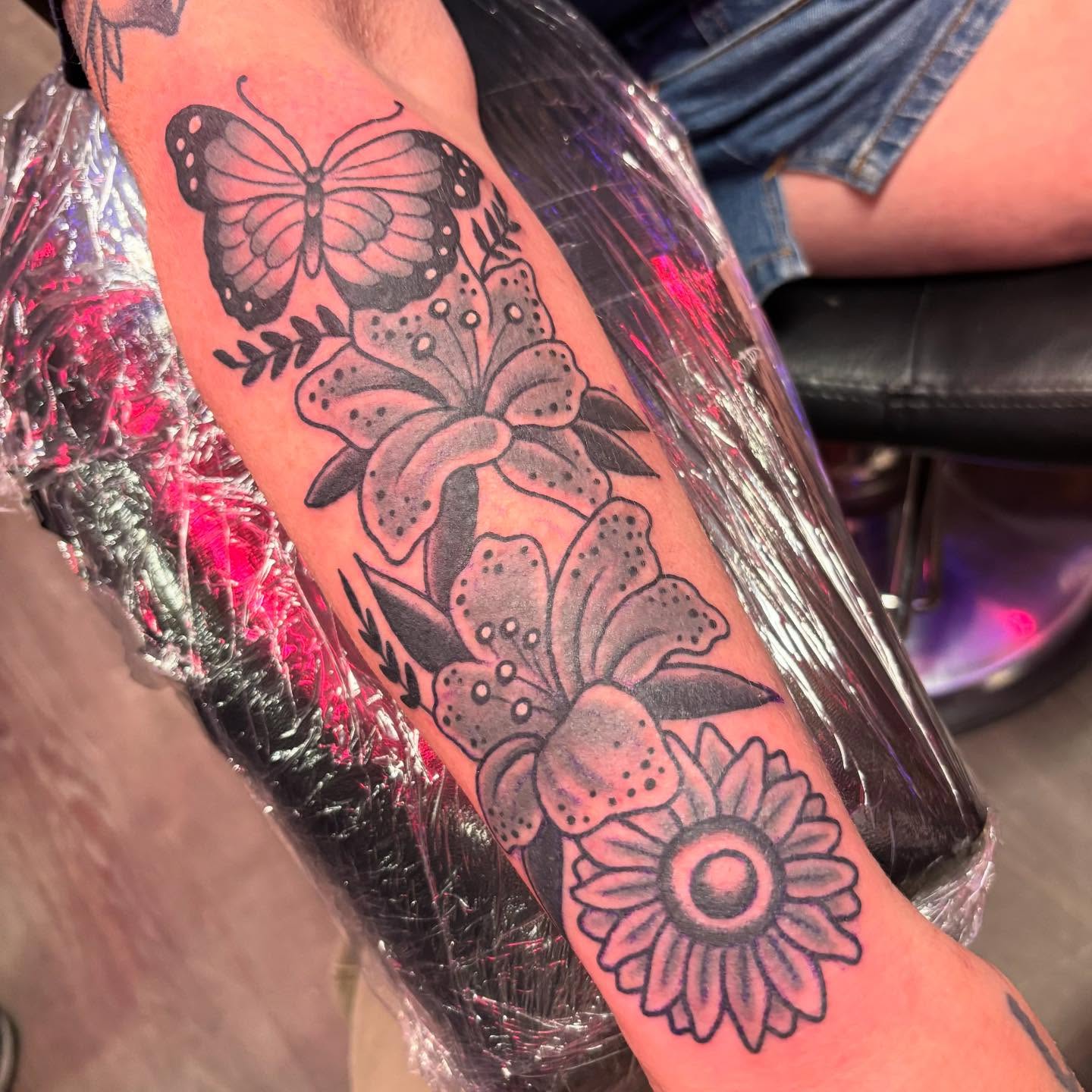 Flowers and butterfly black and grey tattoo on the forearm by @dannydoestattoos