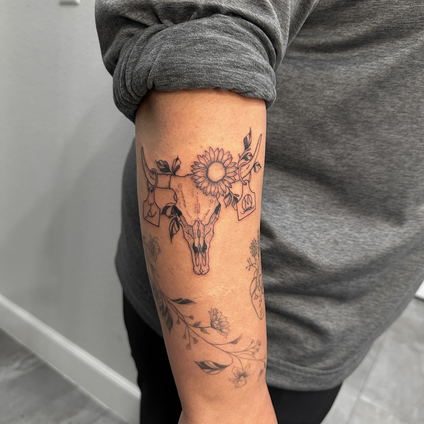 Cow skull with sunflower black and grey tattoo on the forearm by Alex