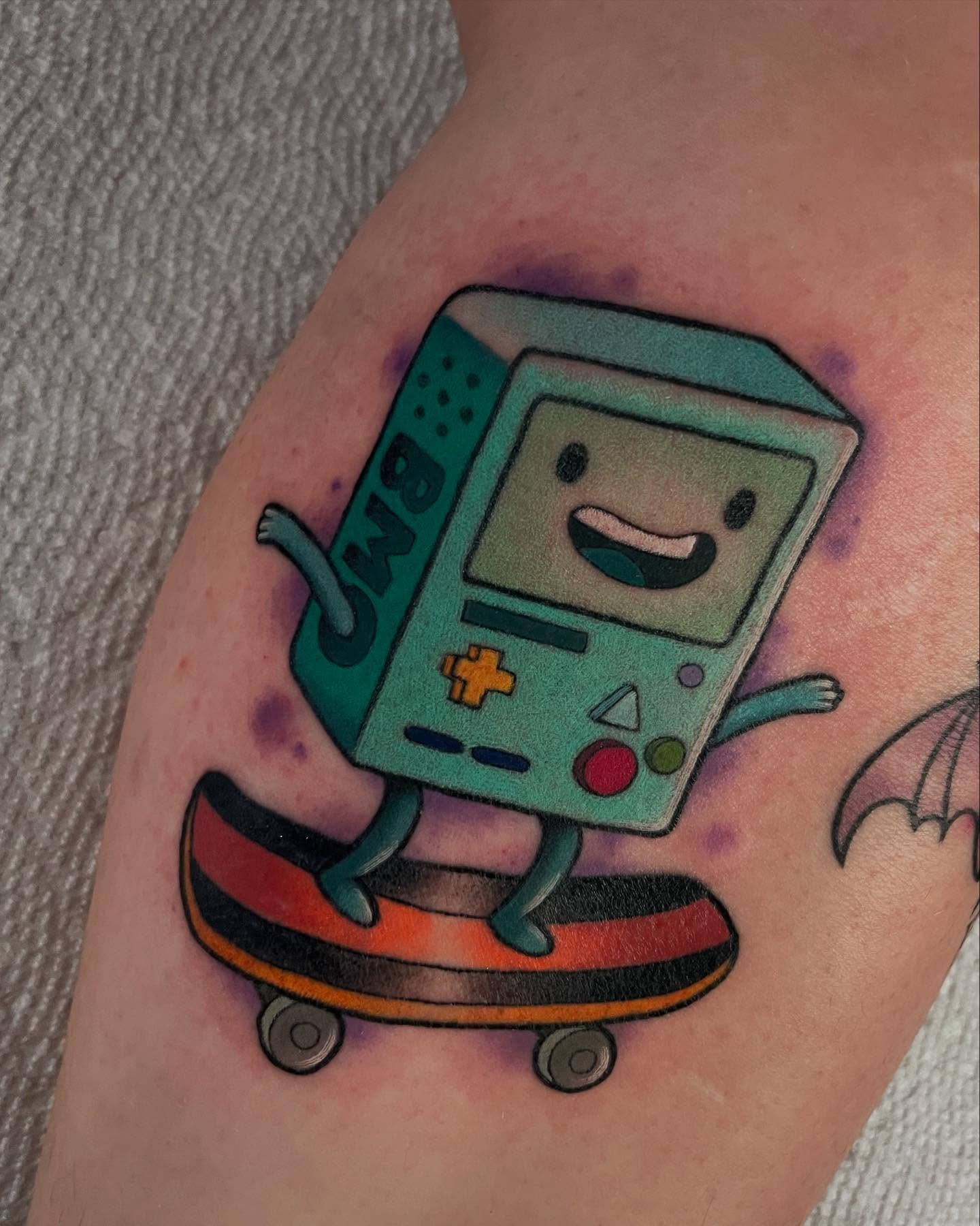 BMO on skateboard new school tattoo on the forearm by Sarah Baldwin