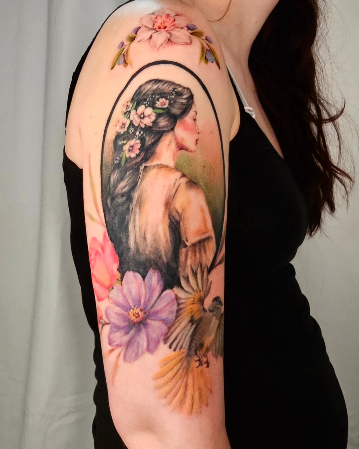 Woman with flowers realism tattoo on the upper arm by Madelynne