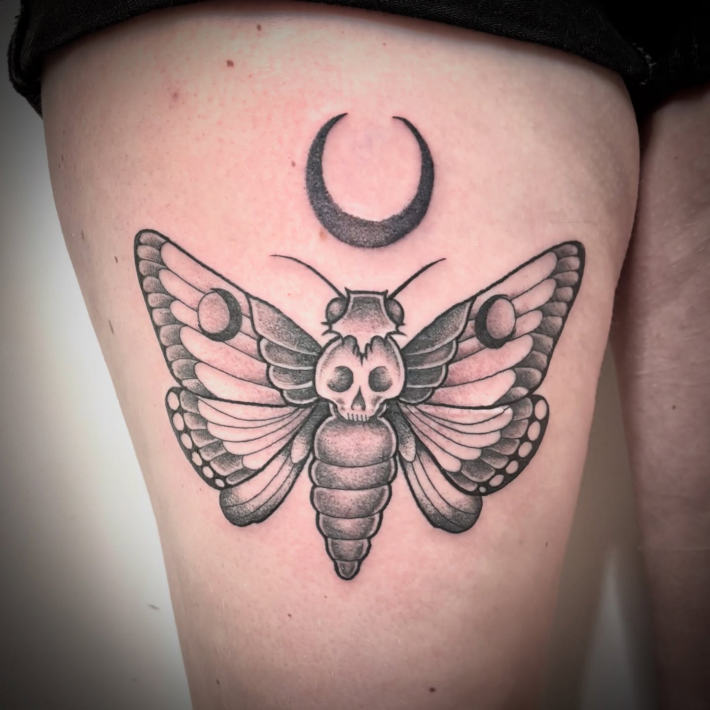 Moth with skull head black and grey tattoo on the thigh by Amber N