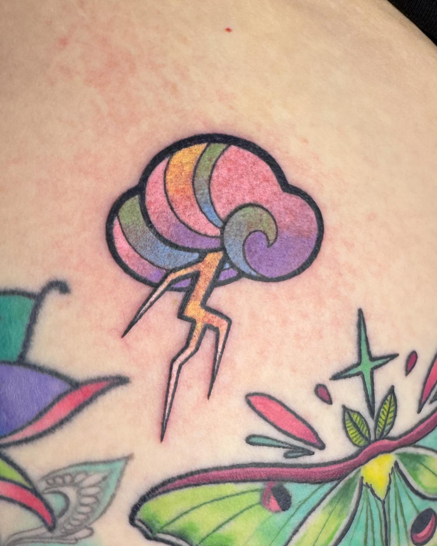 Rainbow cloud with lightning new school tattoo on the torso by Janine Ramos