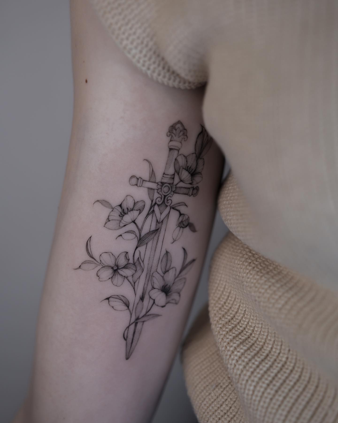 Sword and flowers black and grey tattoo on the forearm by Tattoo artist in Boston