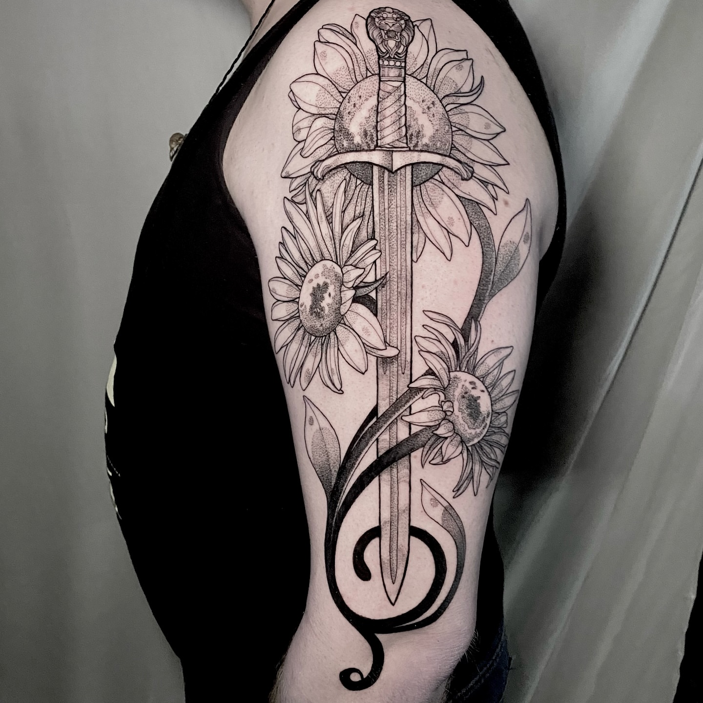 Sunflower and sword geometric tattoo on the upper arm by Rowan Starr