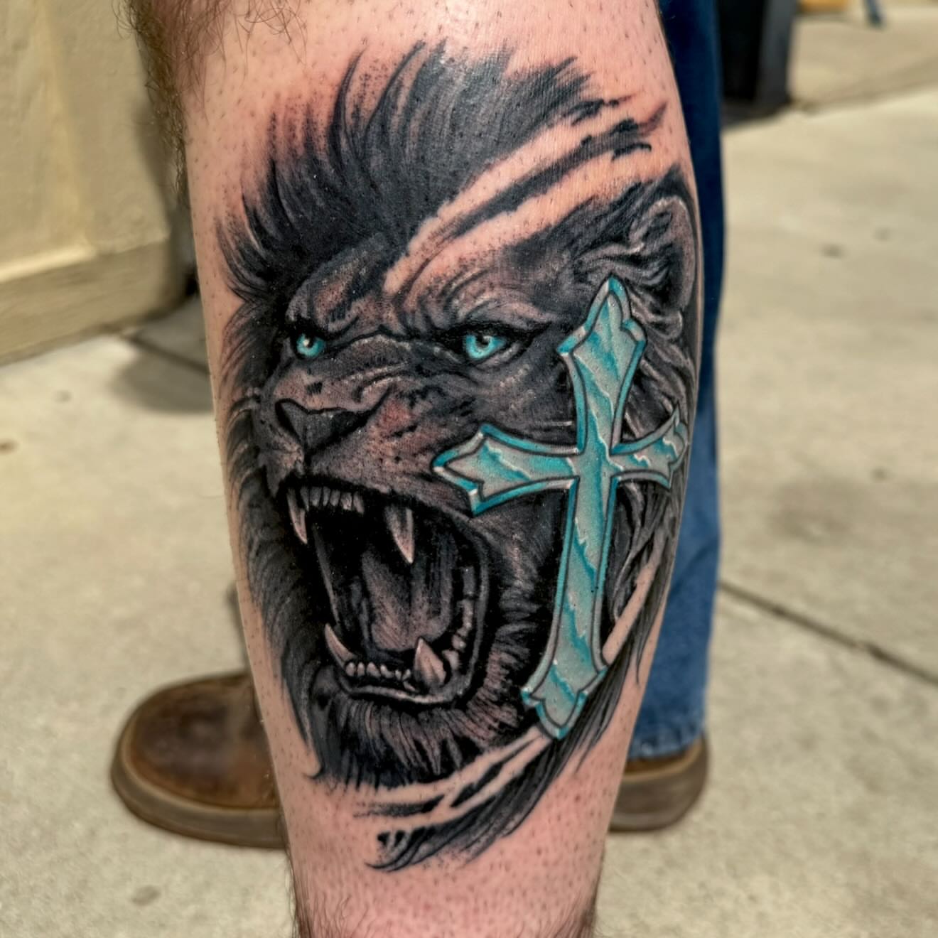 Angry lion with cross realism tattoo on the calf by Michael Latendresse