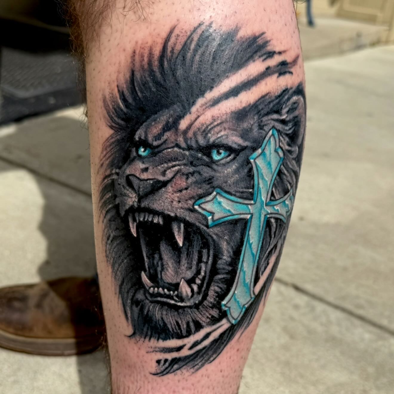 Roaring lion with cross realism tattoo on the forearm by Michael Latendresse