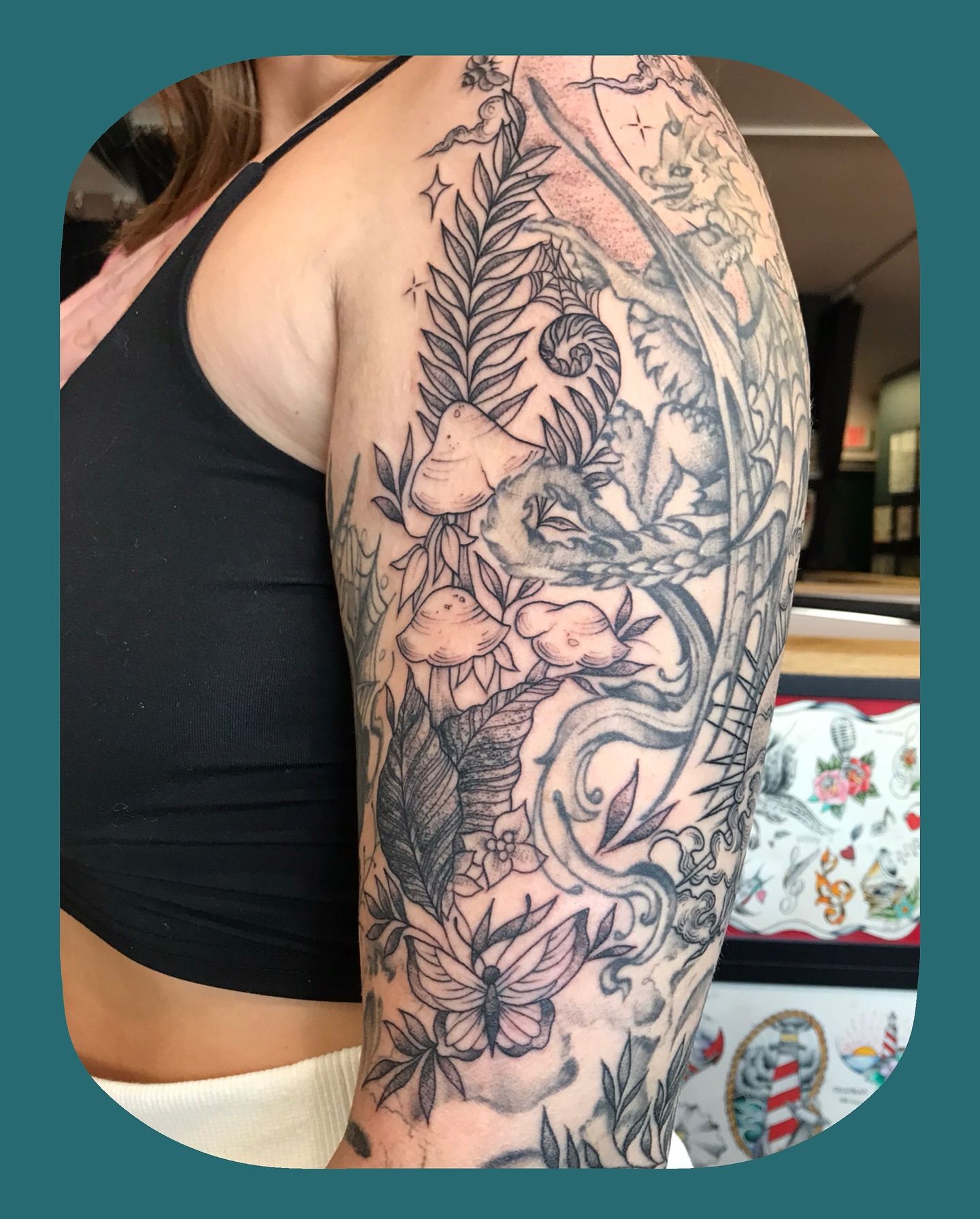 Mythical creature and floral black and grey tattoo on the upper arm by Chris Chapman