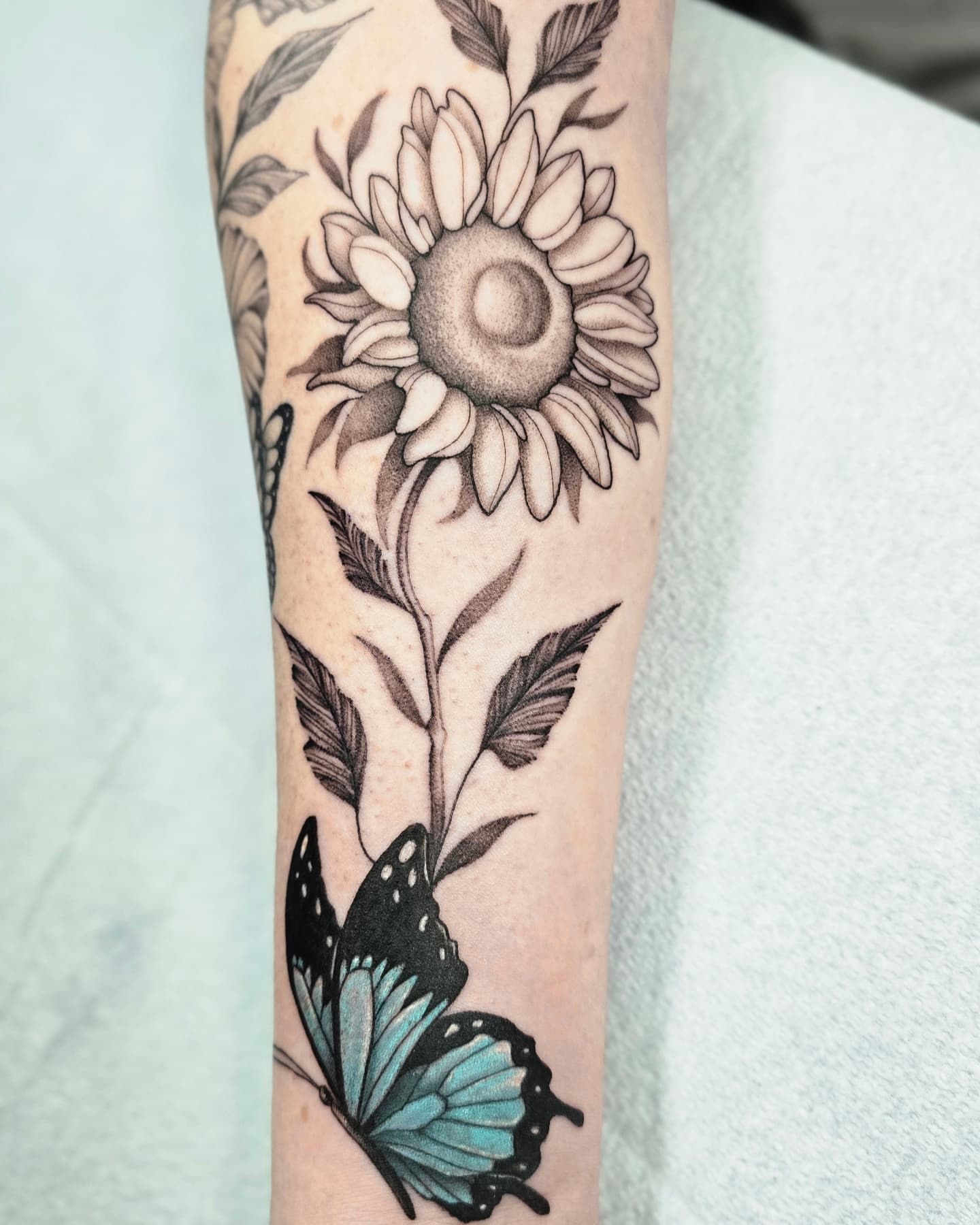Sunflower and butterfly black and grey tattoo on the forearm by Jake Barney