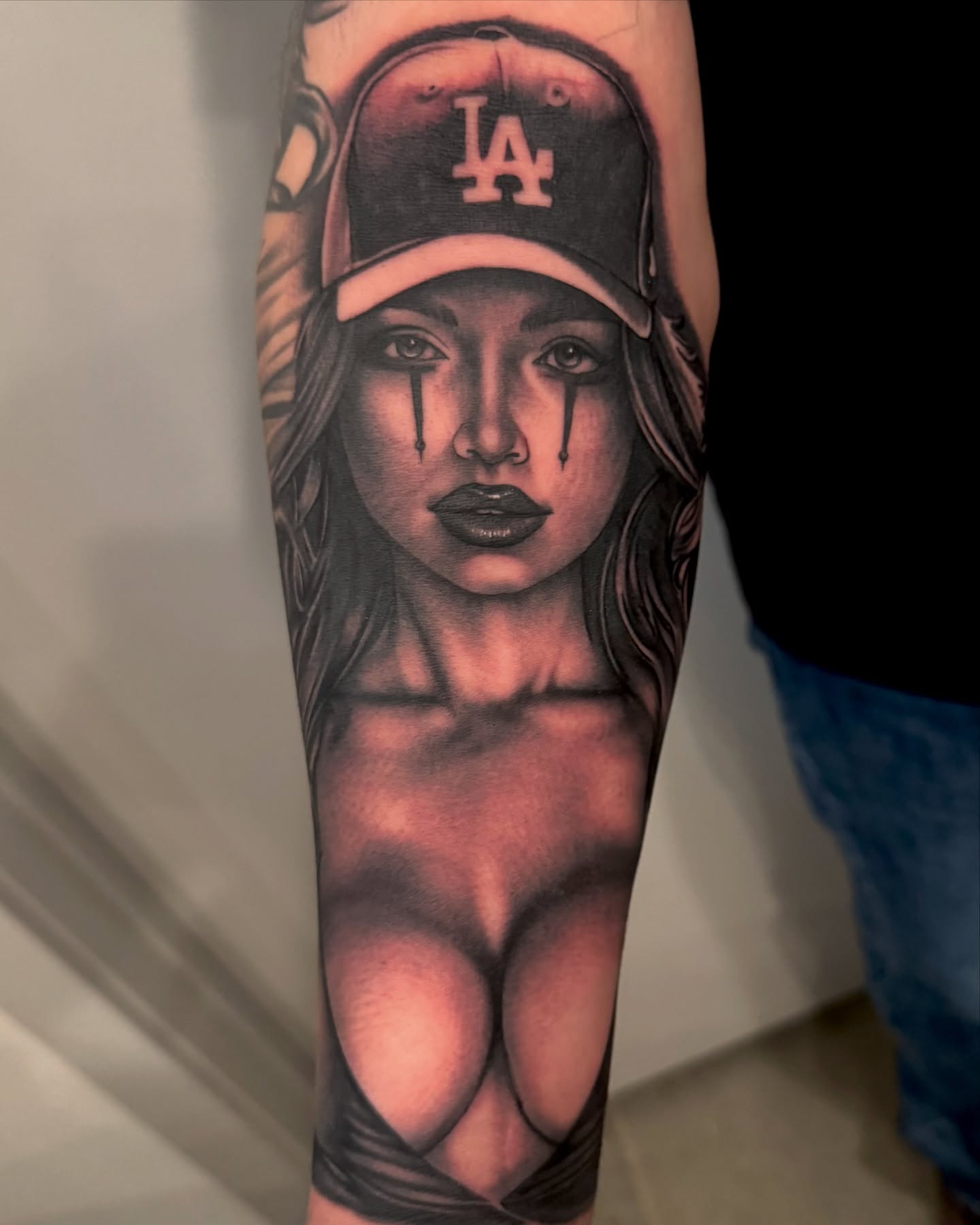 Woman wearing LA cap realism tattoo on the forearm by Gabriel Quintana “Q”