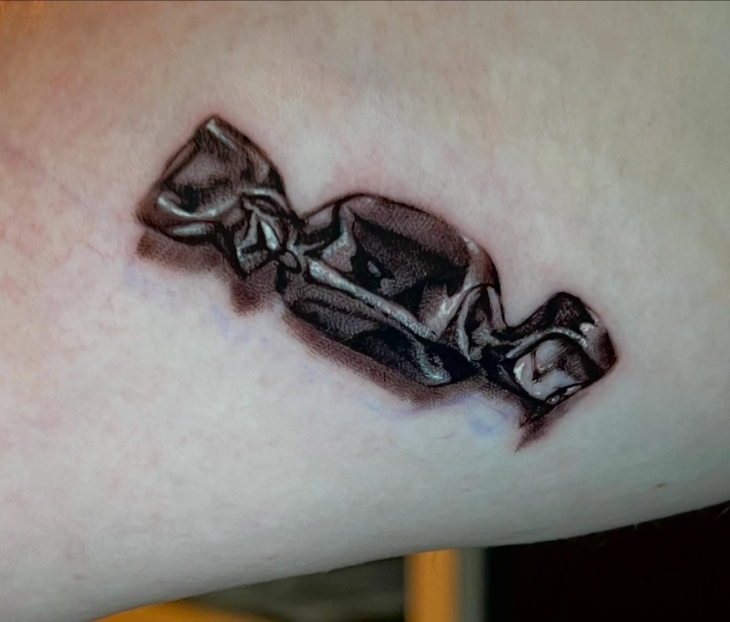 Candy wrapper black and grey tattoo on the forearm by Matthew Arguello