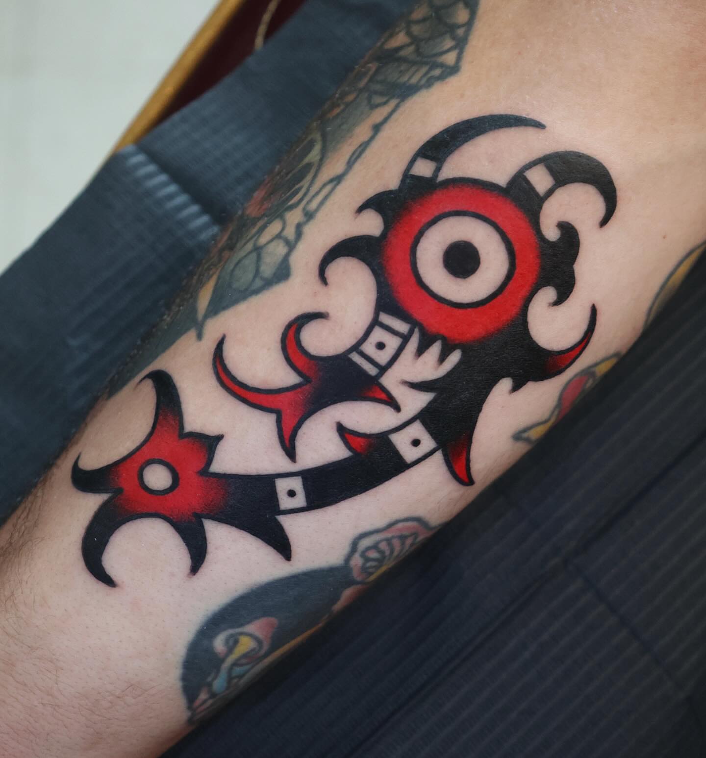 Red and black mask geometric tattoo on the forearm by Big Al