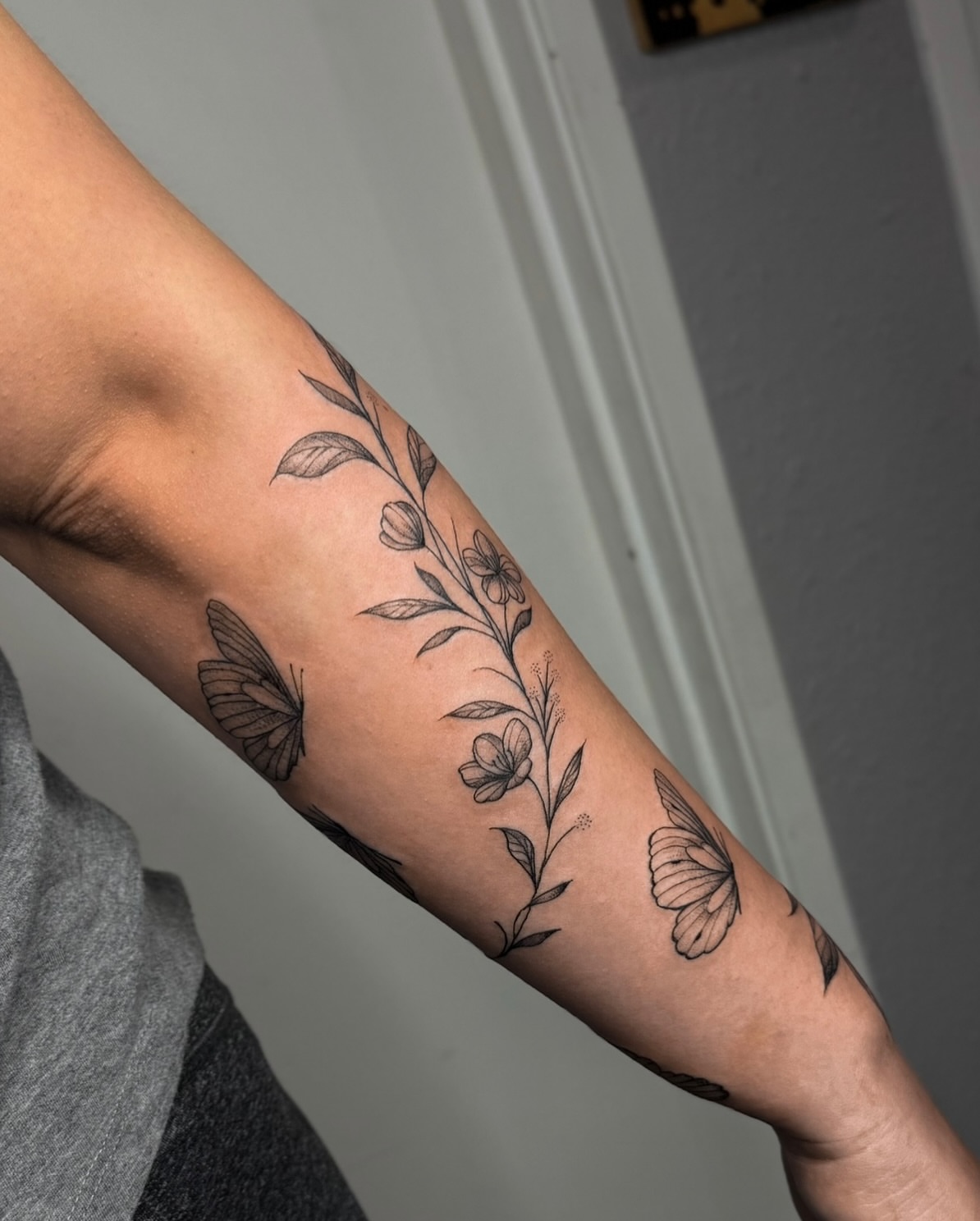 Floral and butterfly black and grey tattoo on the forearm by Dee, San Diego, California