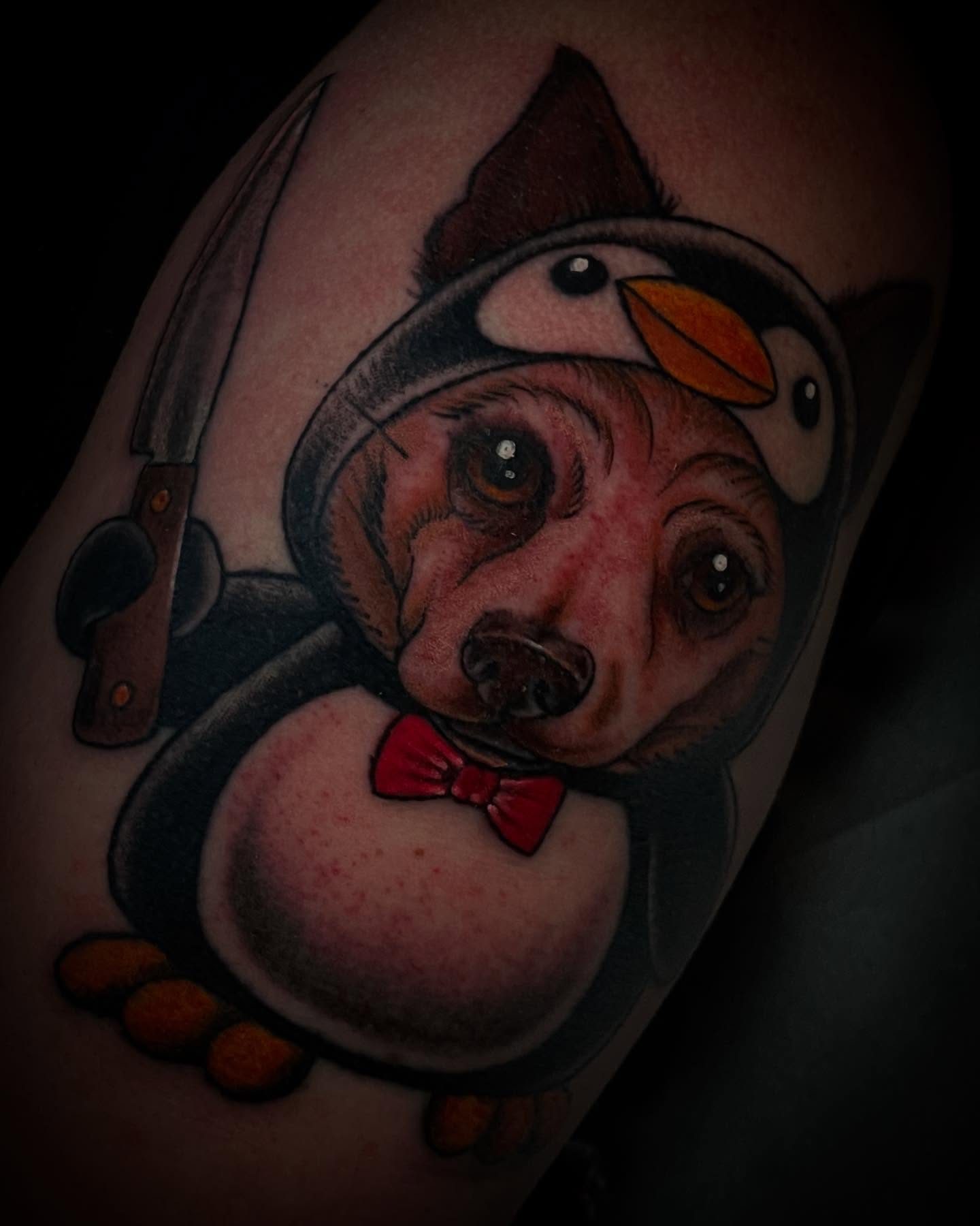 Penguin with dog head realism tattoo on the forearm by Madison ‘Maddog’ Stewart