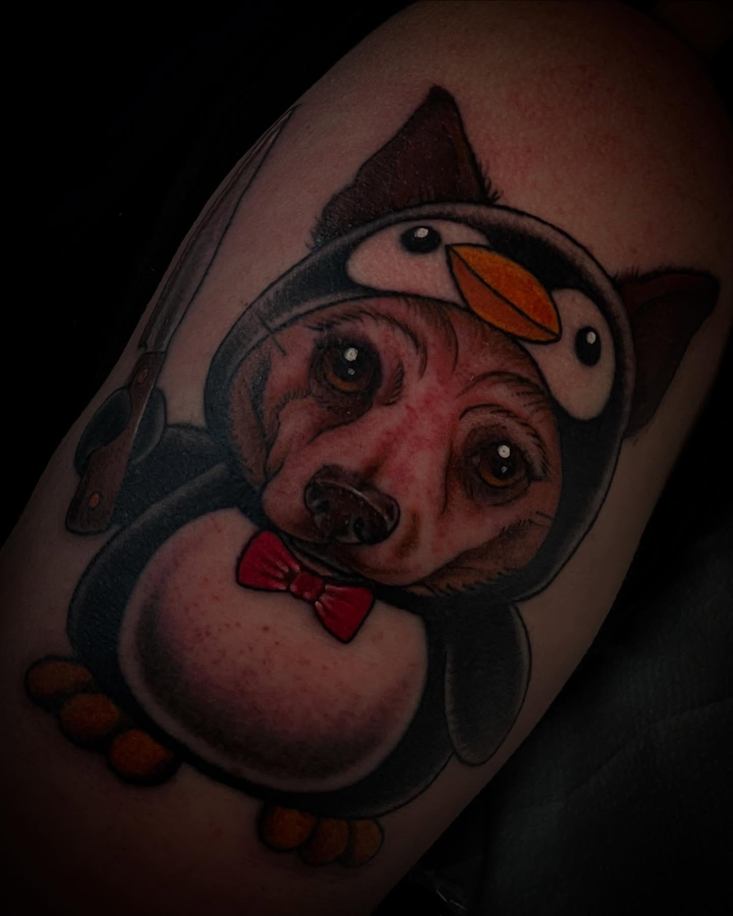 Dog wearing penguin costume realism tattoo on the forearm by Madison ‘Maddog’ Stewart