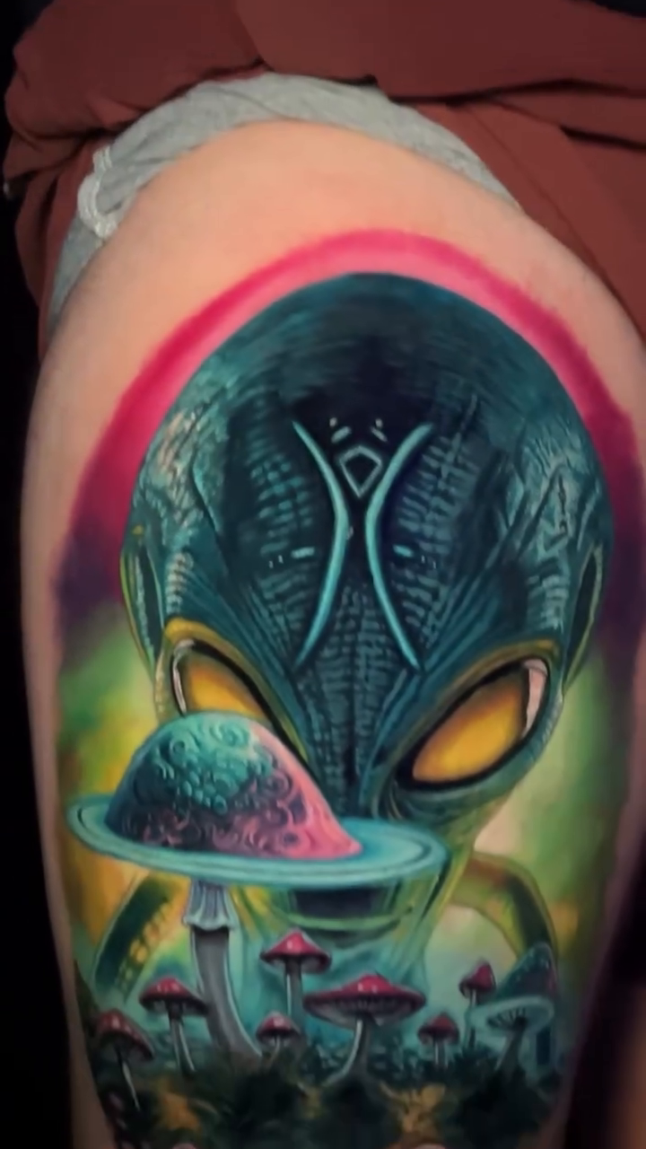 Alien holding a mushroom surrealism tattoo on the upper arm by Sean Foy
