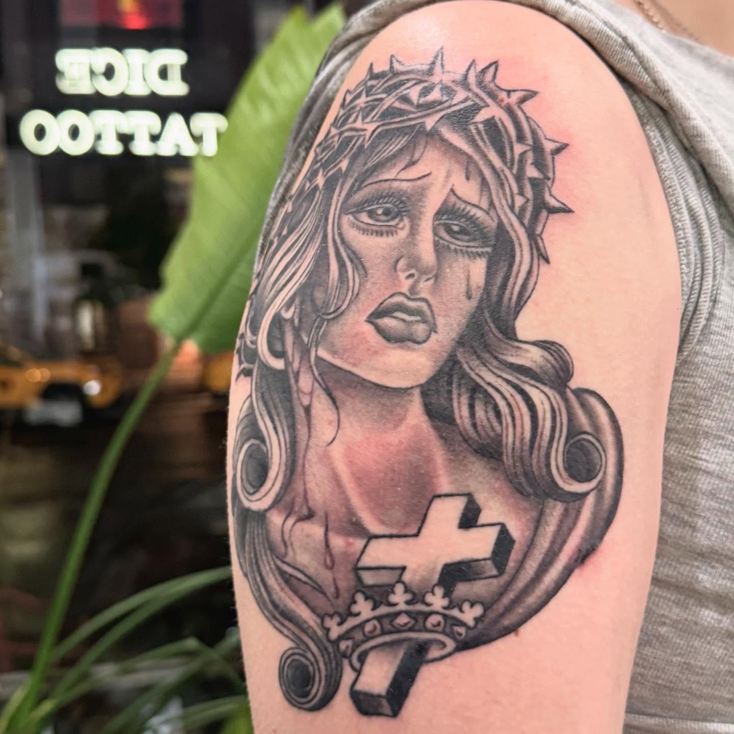 Woman with crown and cross realism tattoo on the shoulder by 𝕯𝖗𝖆𝕶𝖊㋛