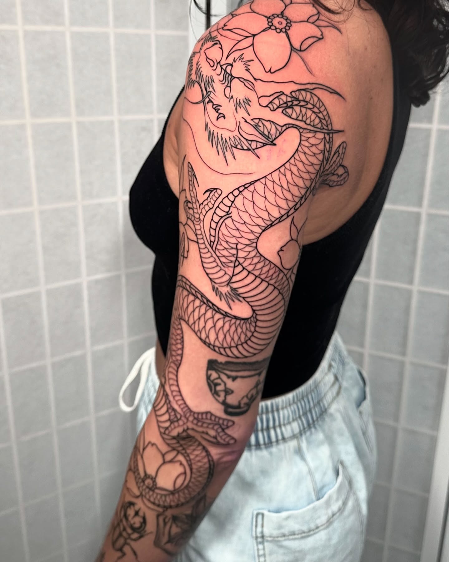 Dragon and flower black and grey tattoo on the upper arm by Henry Gaßner