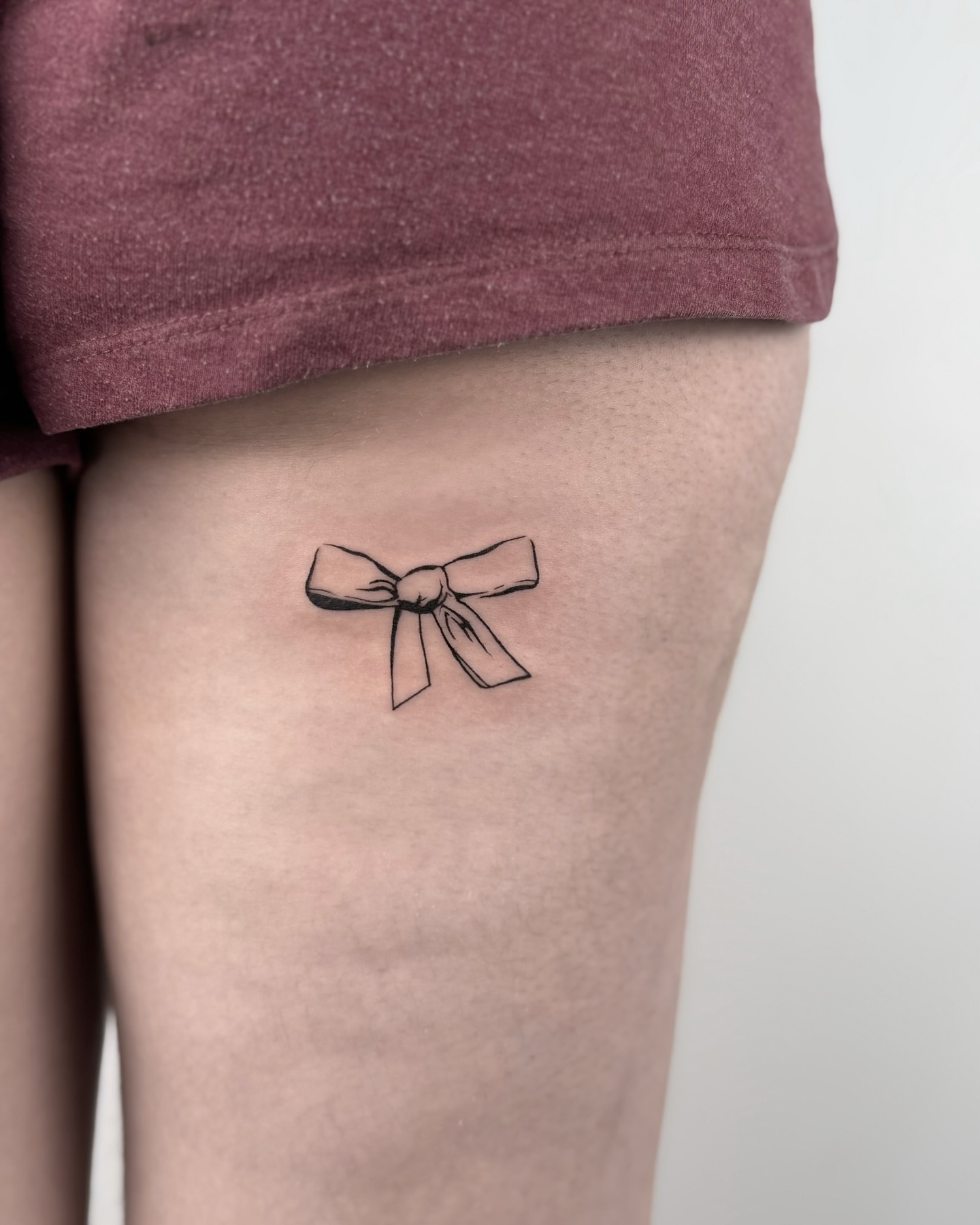 Bow minimalist tattoo on the thigh by Casper Tattoos Toronto