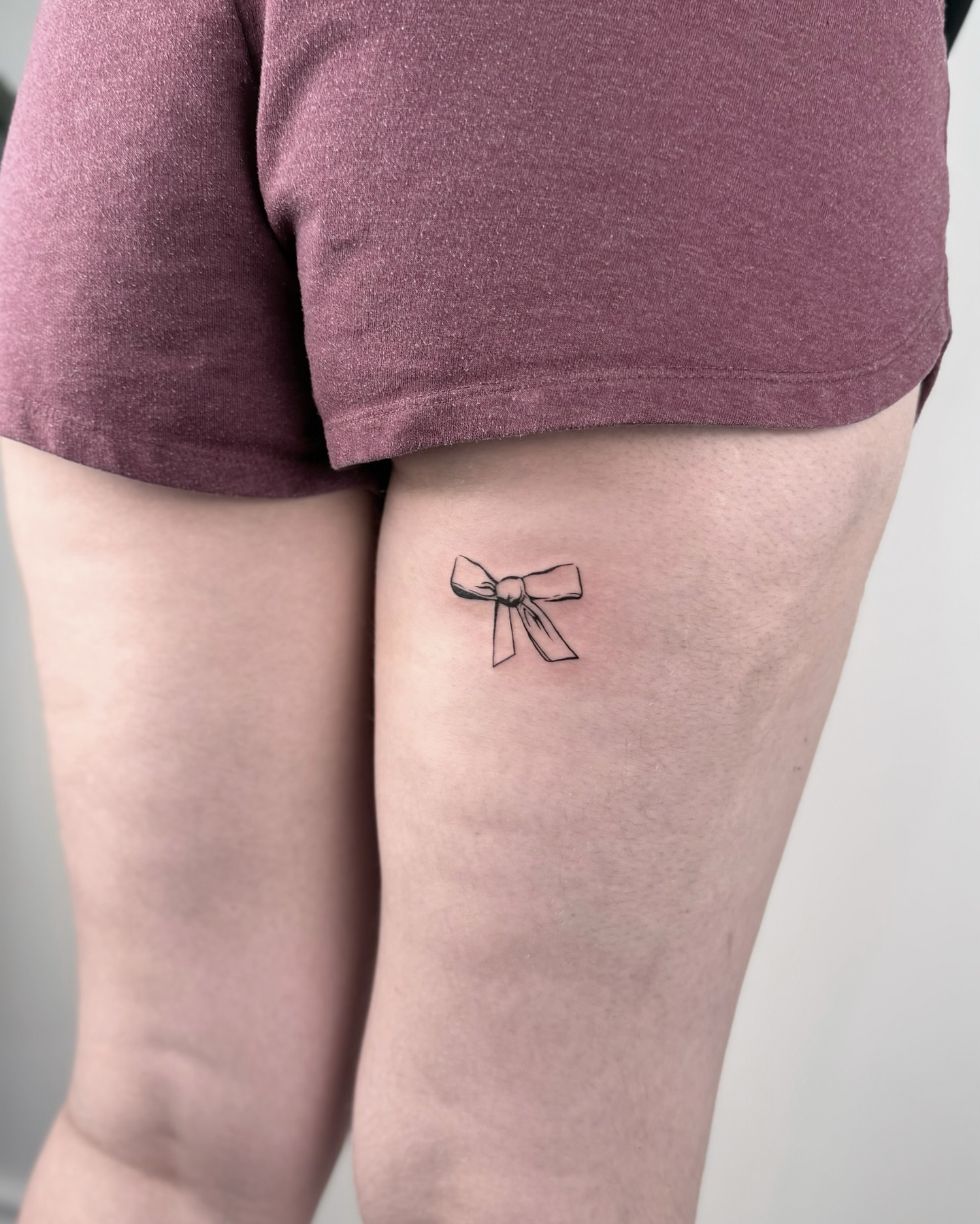 Bow fine line tattoo on the thigh by Casper Tattoos Toronto
