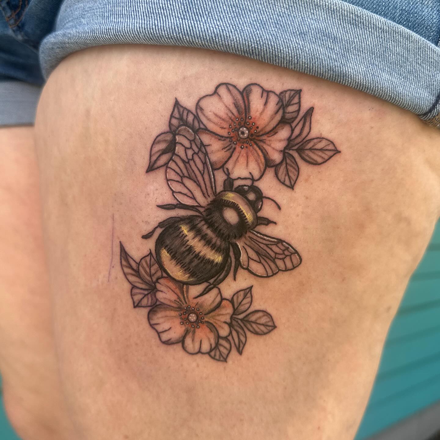 Bee and flowers realism tattoo on the thigh by Mika'la Berry