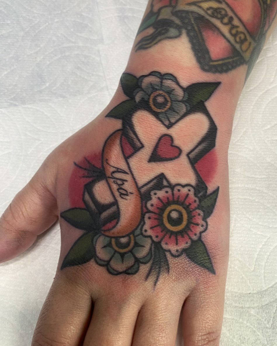 Cross with floral elements American traditional tattoo on the hand by Lindsey Cam Van