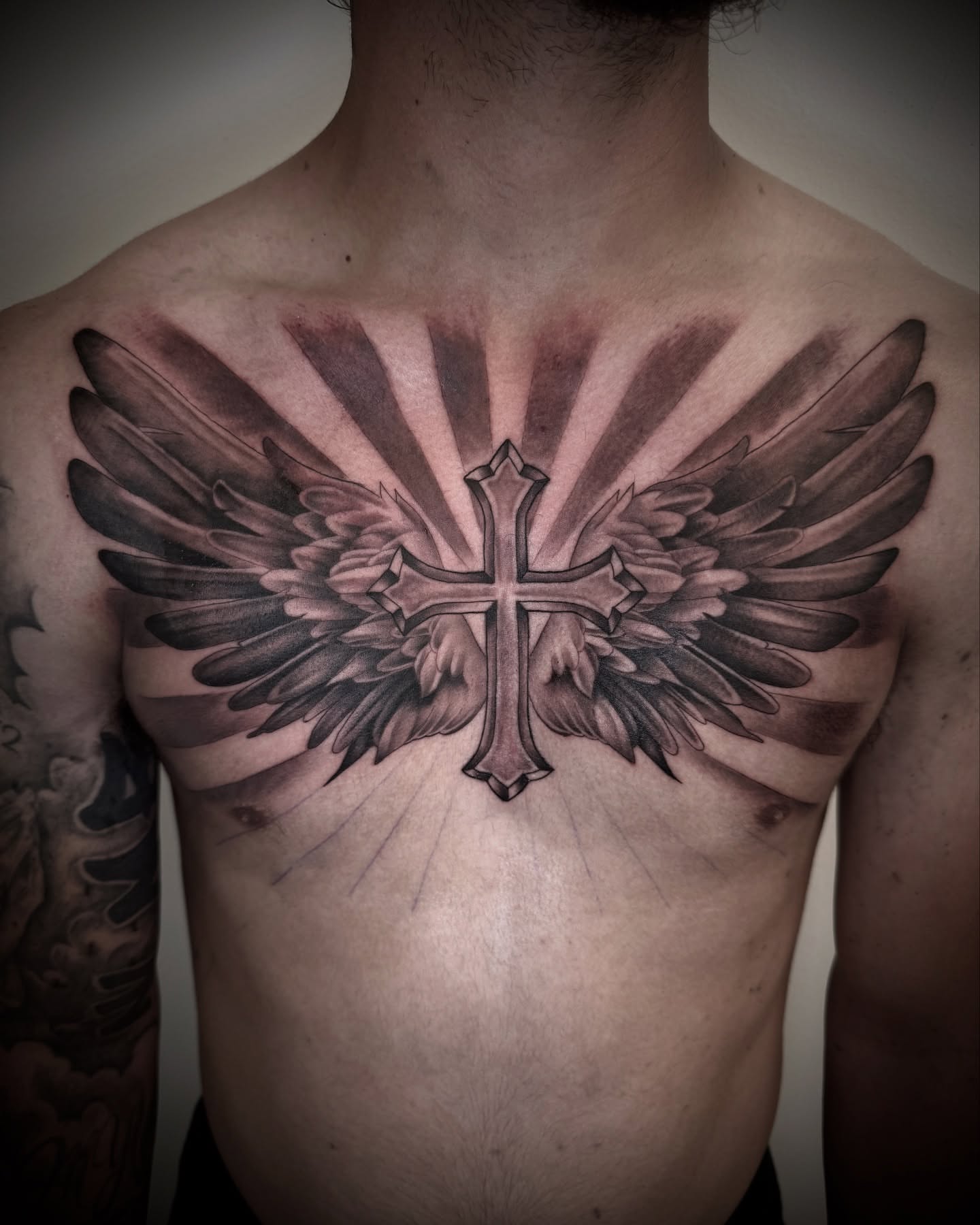 Cross with wings black and grey tattoo on the chest by Chip