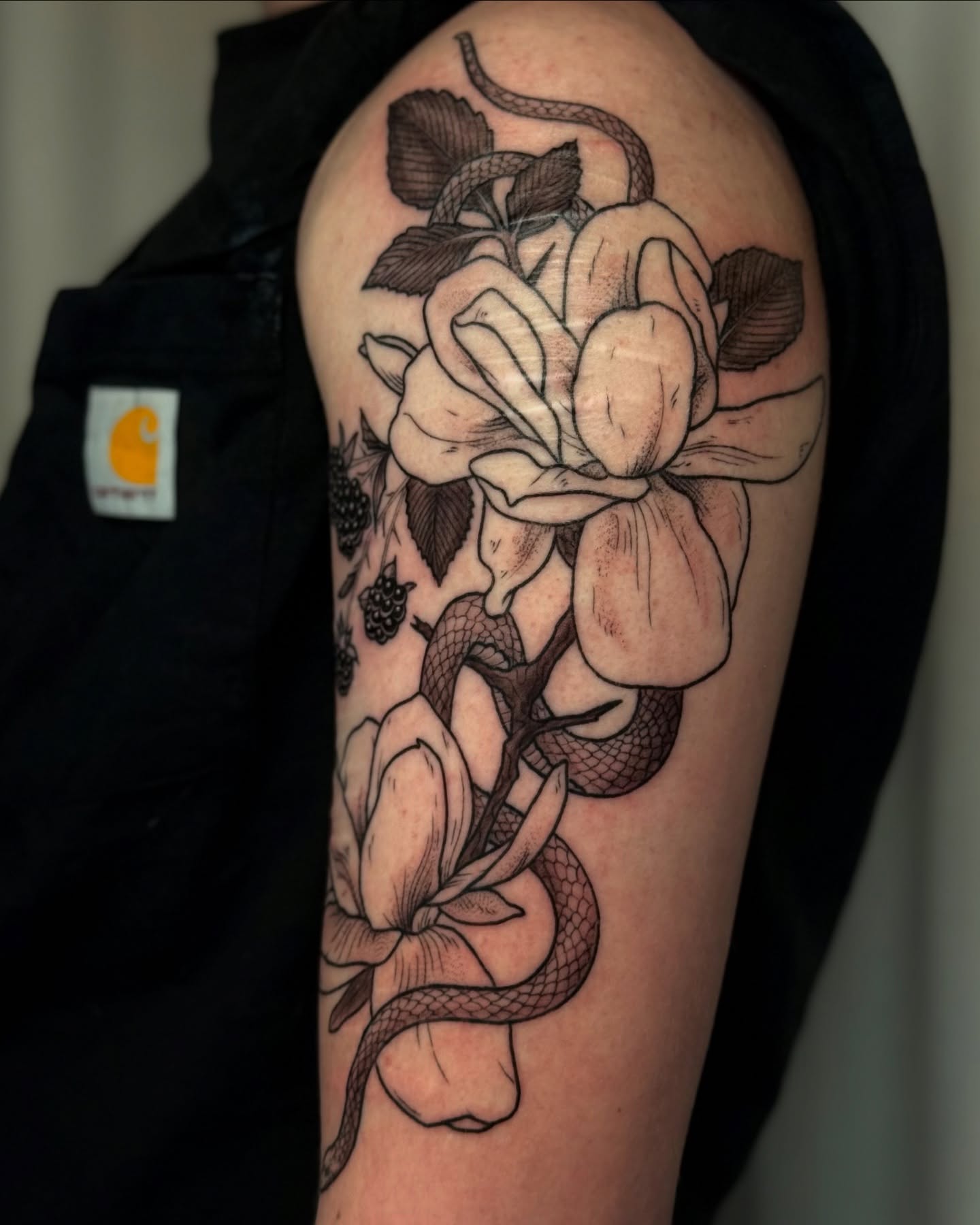 Snake and flowers realism tattoo on the upper arm by Cooper
