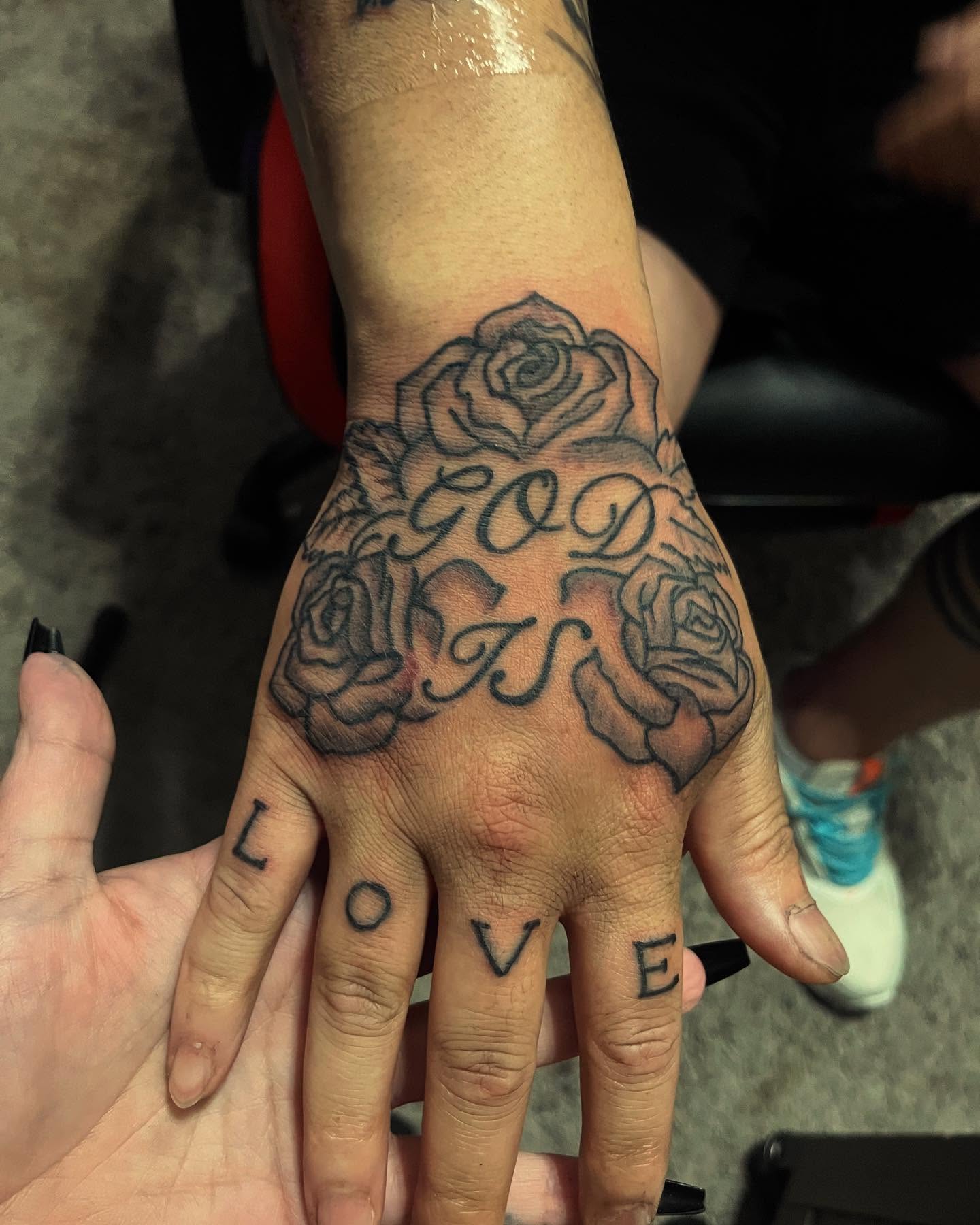 Roses and 'God Is Love' black and grey tattoo on the hand by Anna DeLuna