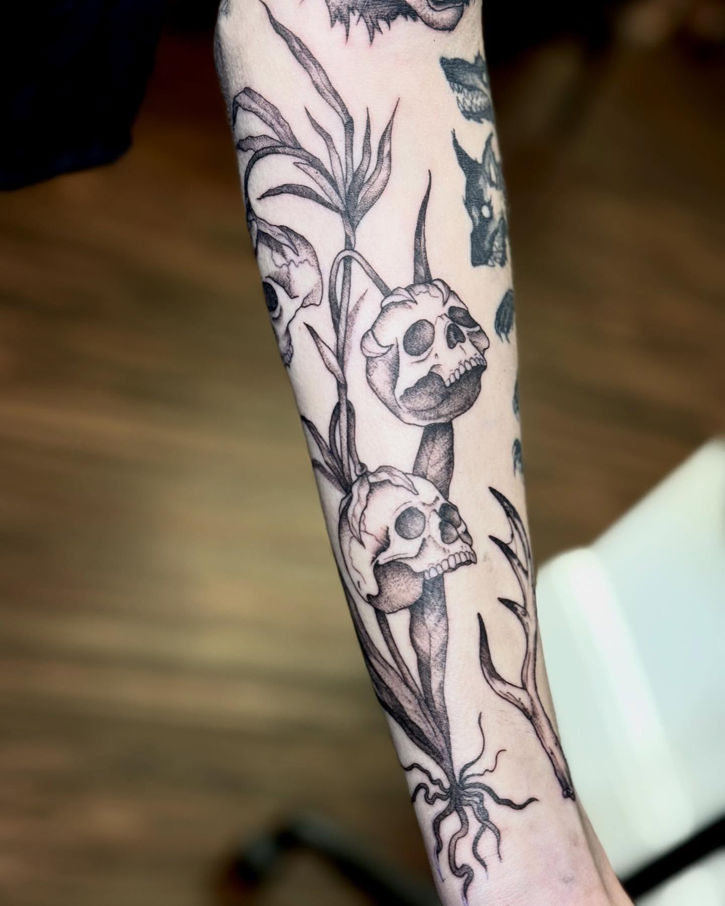 Skulls and plants black and grey tattoo on the forearm by Katie Stacy
