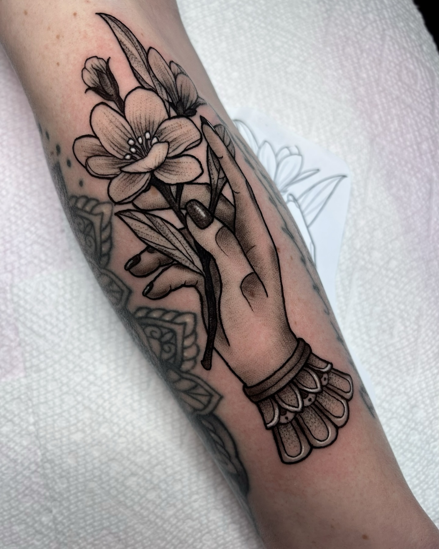 Hand holding flowers black and grey tattoo on the forearm by Melissa Brown