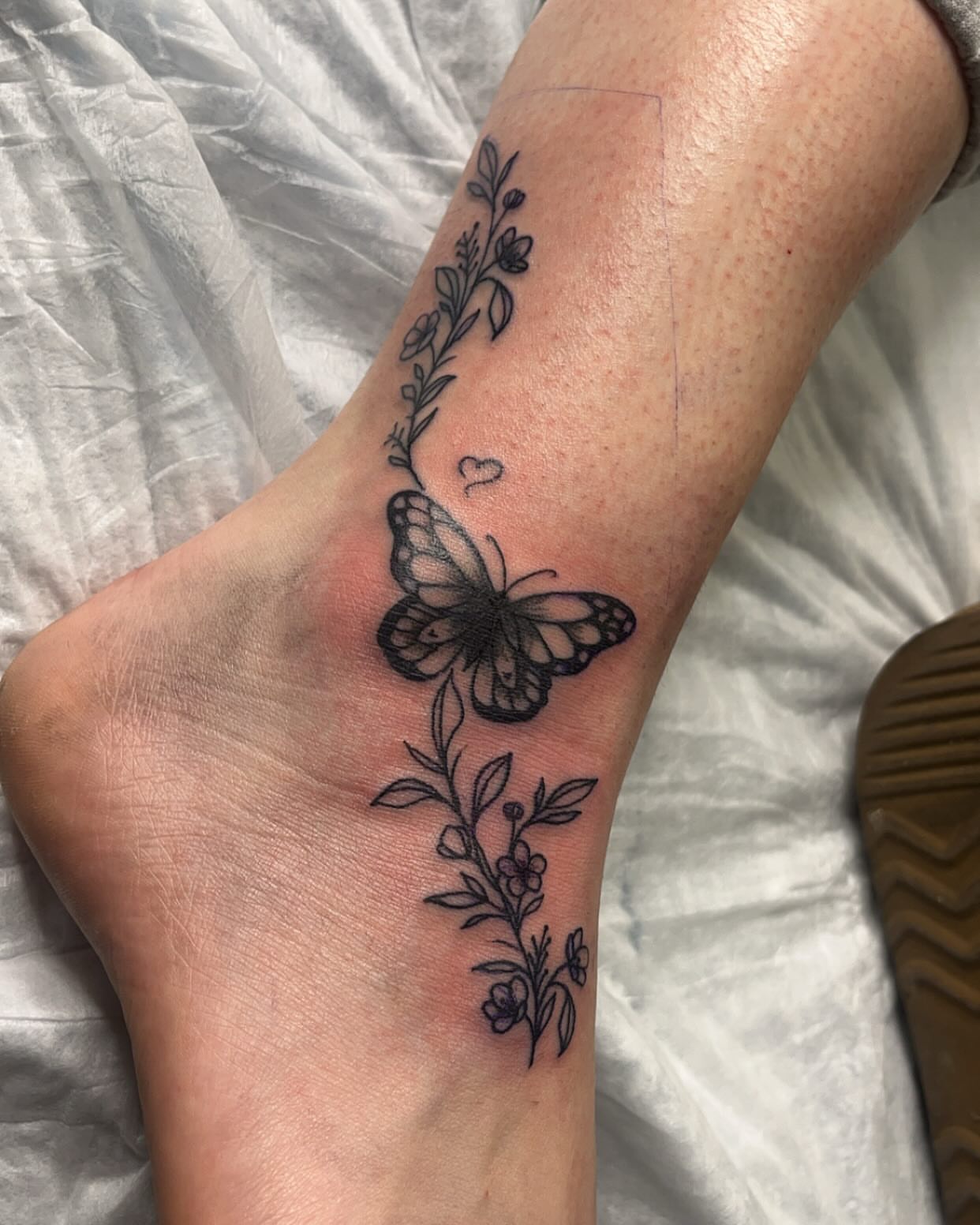 Butterfly and floral vine black and grey tattoo on the foot by Alesia