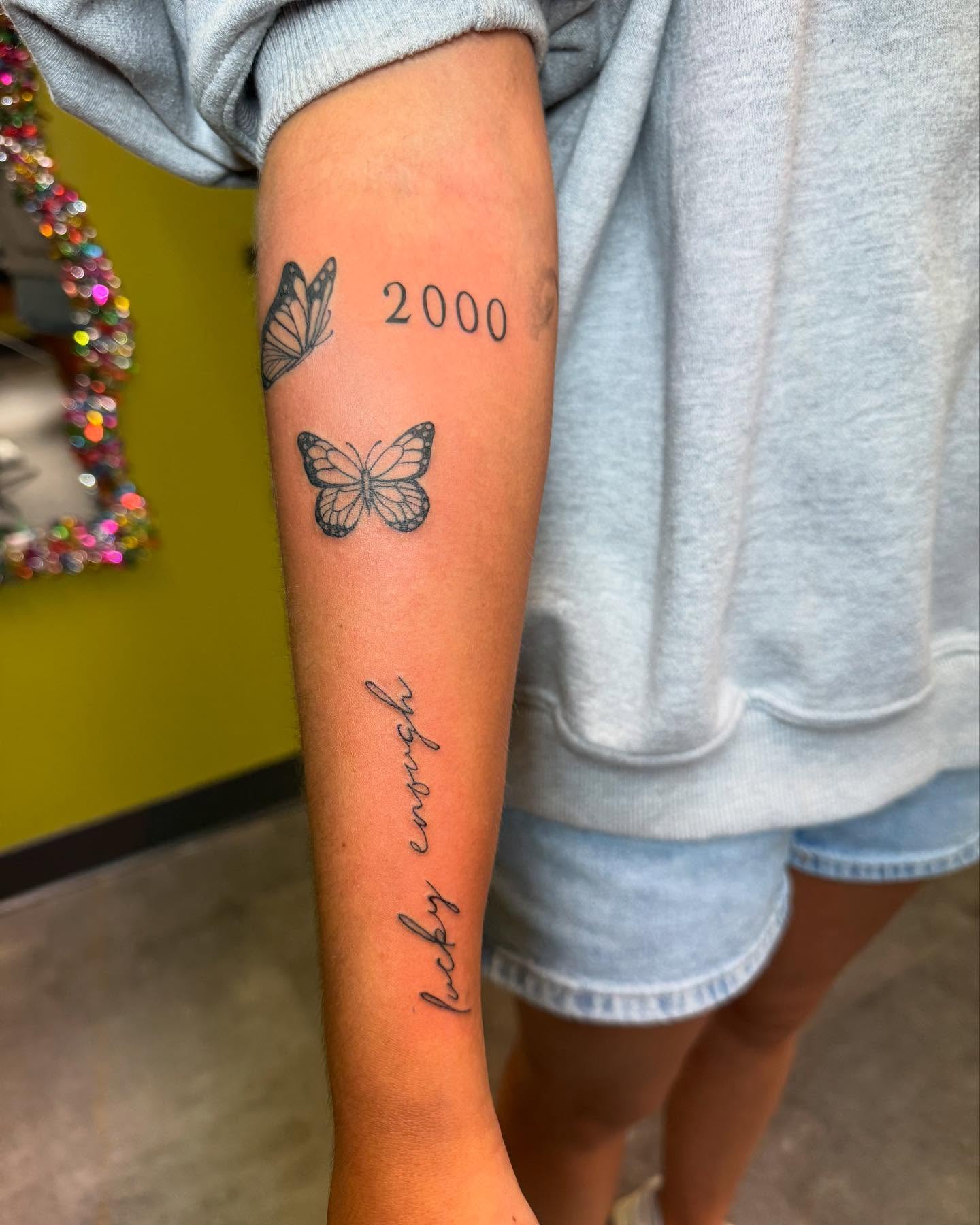 Butterflies and year black and grey tattoo on the forearm by 𝗞𝗮𝘁 𝗕𝗹𝗮𝗻𝗸𝗲𝗻𝘀𝗵𝗶𝗽
