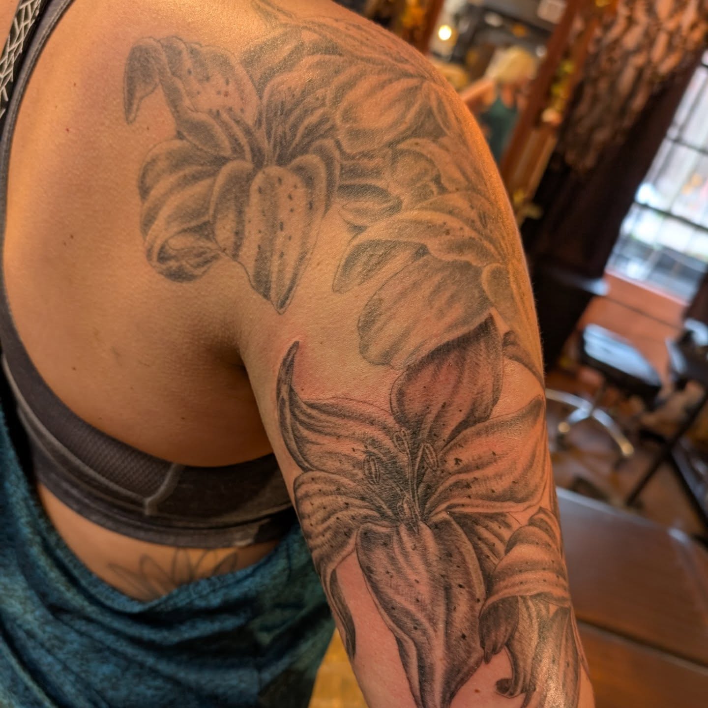 Lily black and grey tattoo on the upper arm by Cat