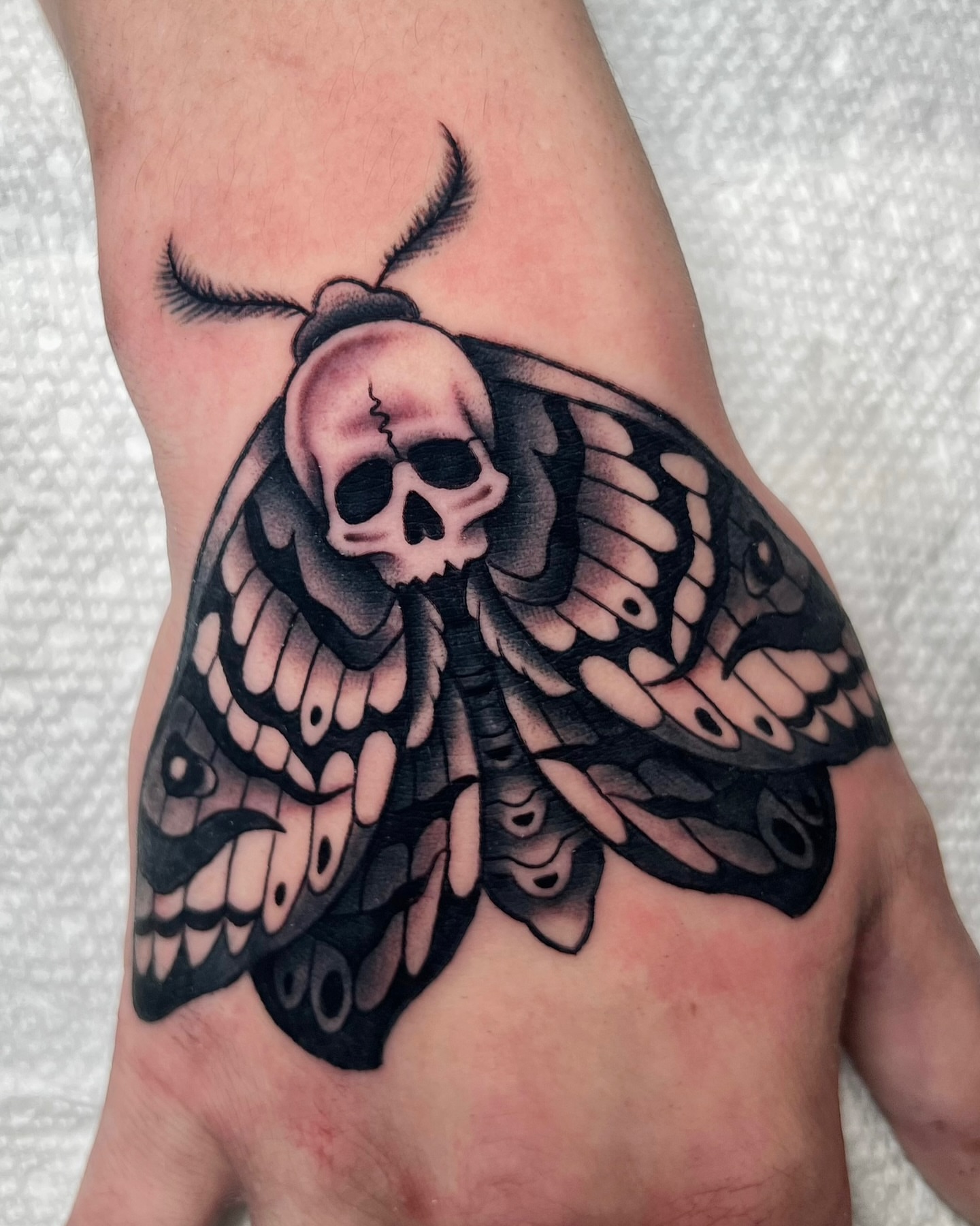 Moth with skull head black and grey tattoo on the hand by Nick Monastra