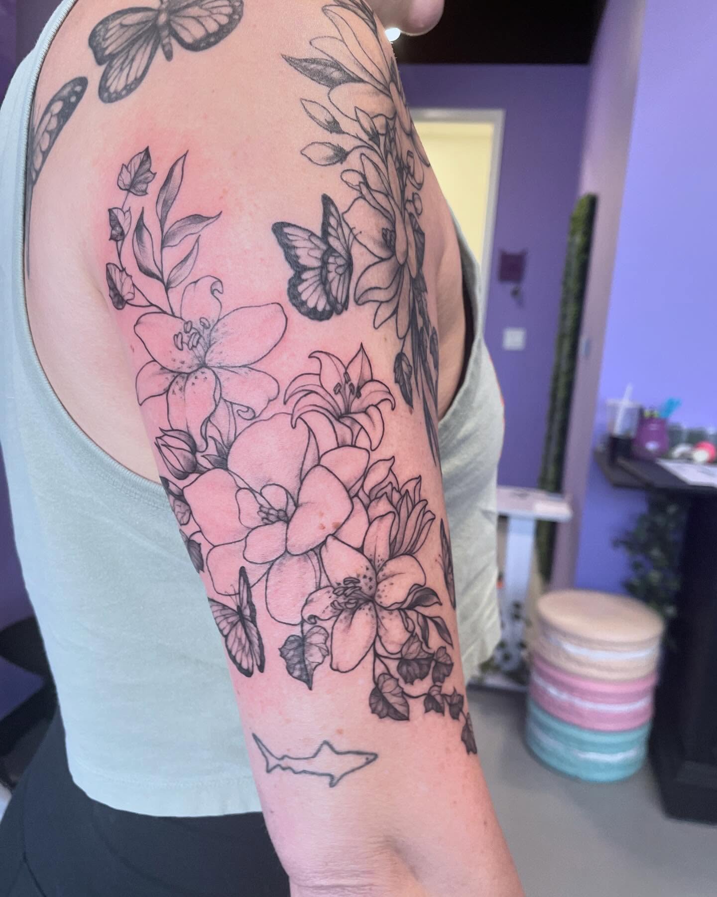 Flowers and butterflies black and grey tattoo on the upper arm by Christin Baumgart