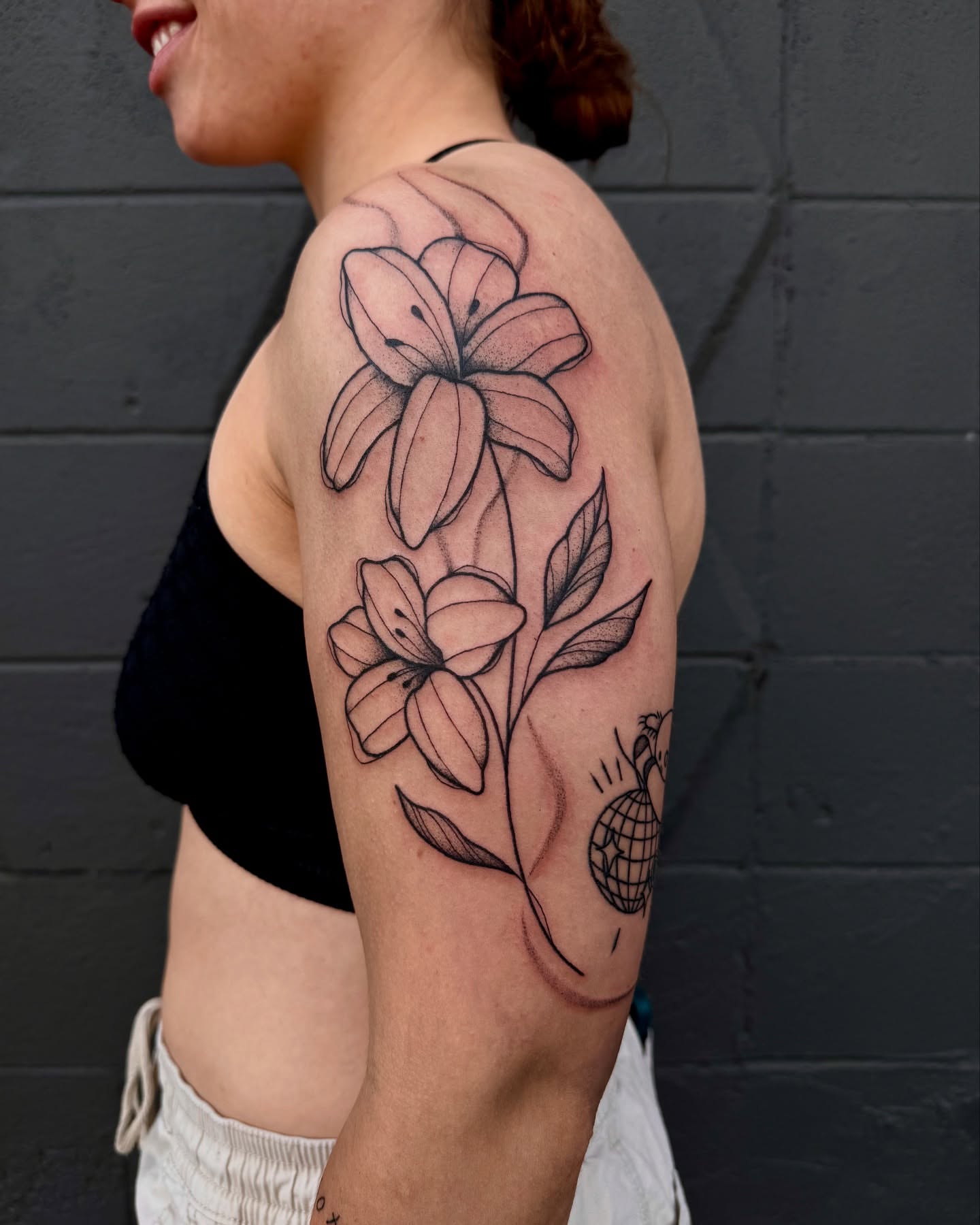 Lilies black and grey tattoo on the upper arm by Mazie