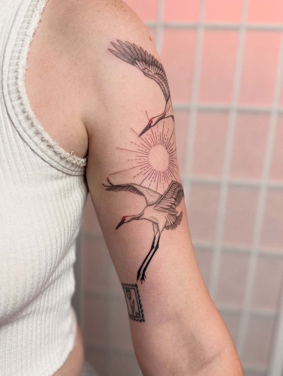 Cranes and sun fine line tattoo on the upper arm by Dama