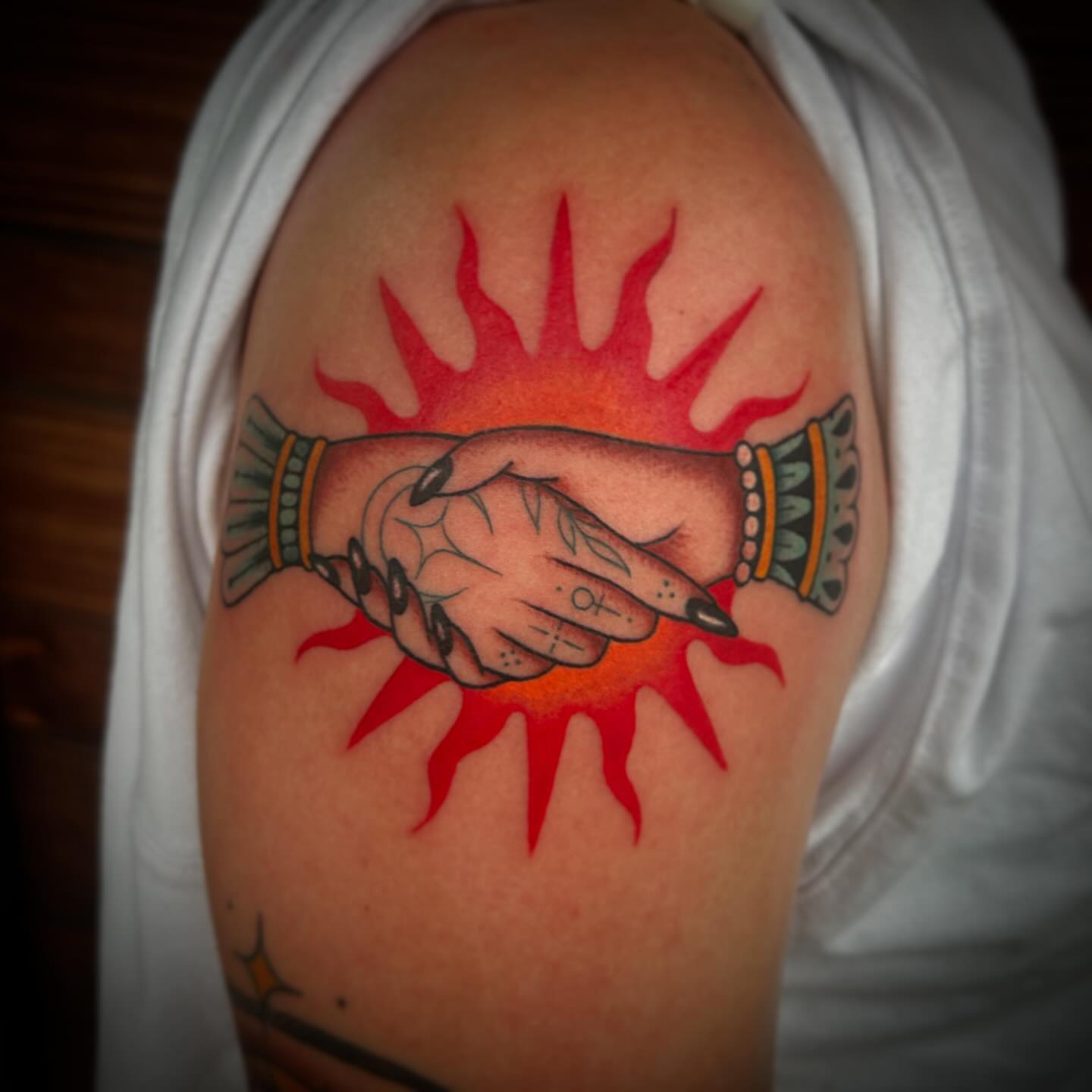Hands and sunburst American traditional tattoo on the shoulder by Kayla Shoffner