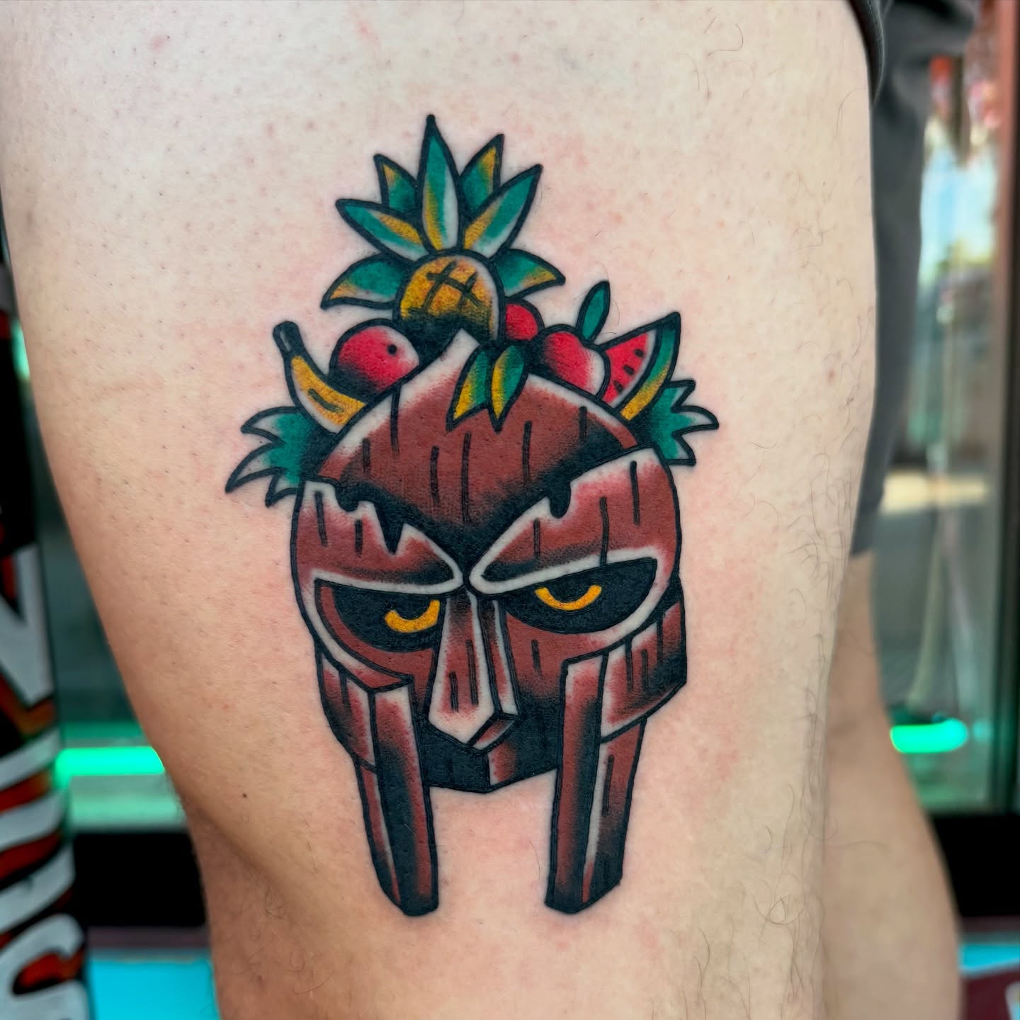 Angry mask with fruits American traditional tattoo on the thigh by Buddy (Holiday) Orr, Las Vegas, Nevada