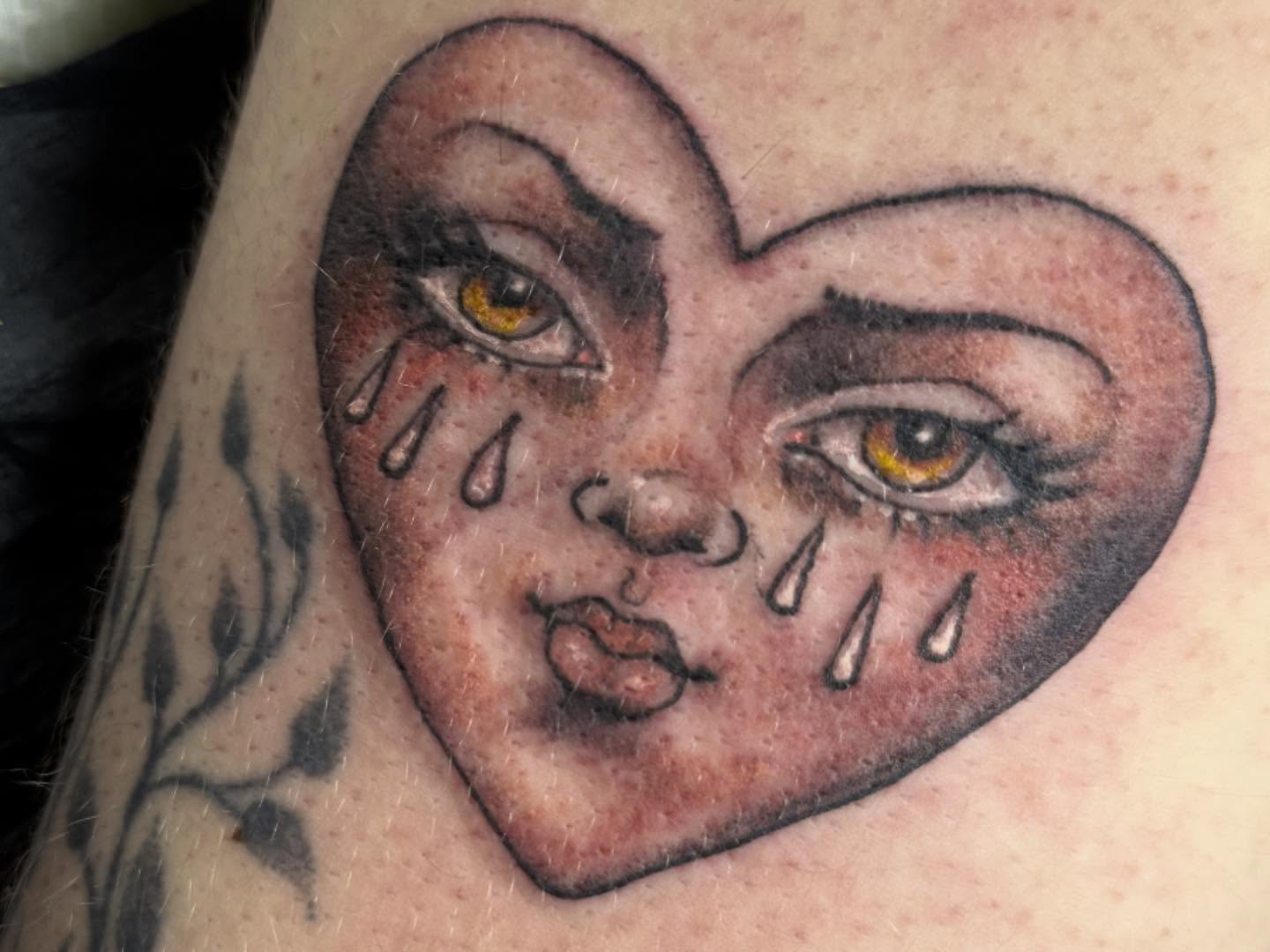 Heart with crying face American traditional tattoo on the forearm by Tattoos By Trish