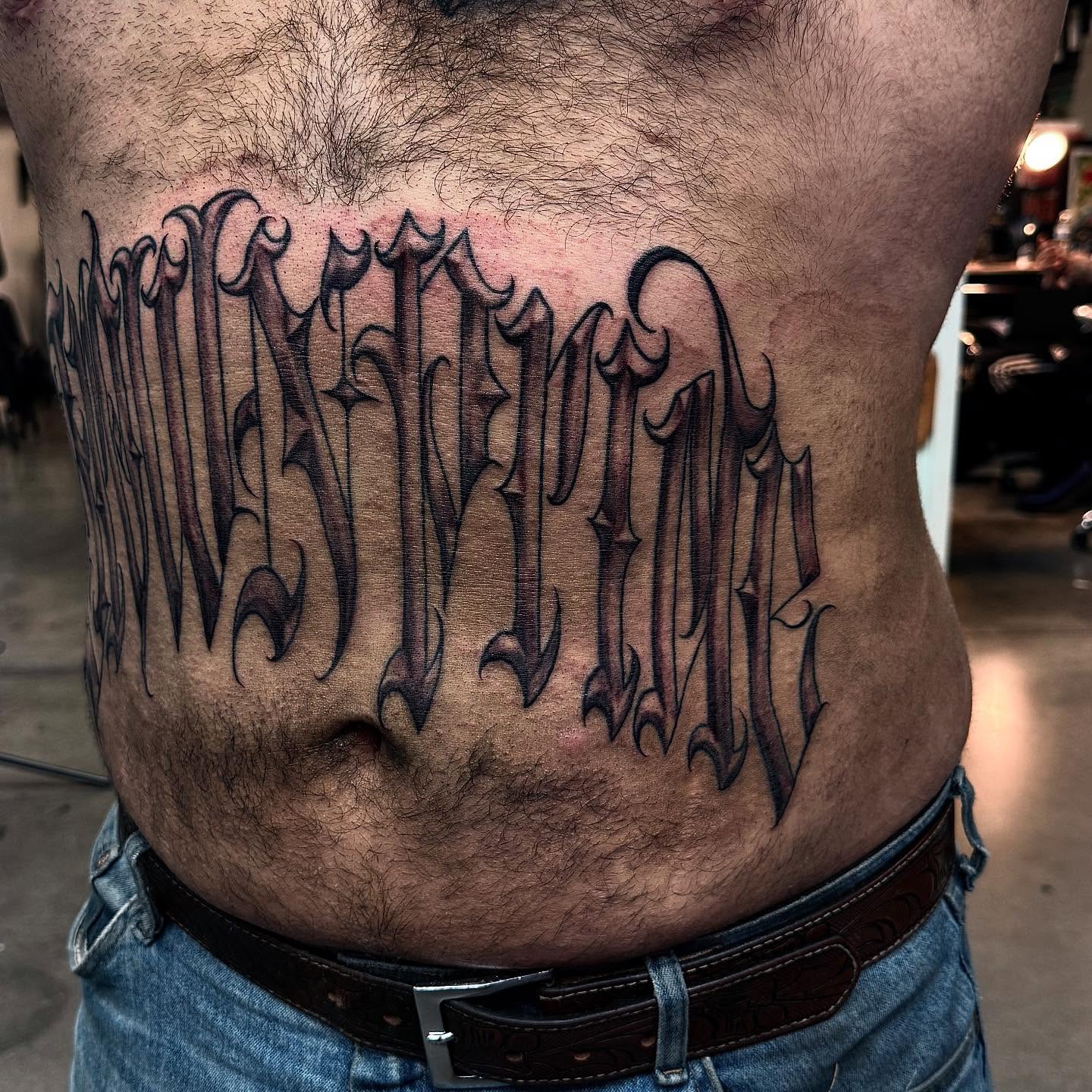 Gothic script lettering script tattoo on the torso by Joey Moreno