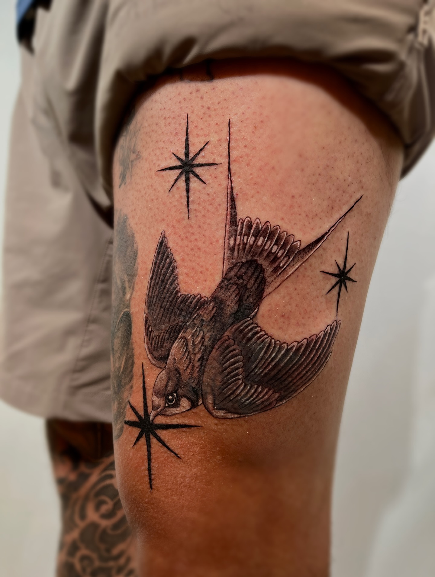 Swallow and stars black and grey tattoo on the thigh by @tattotos