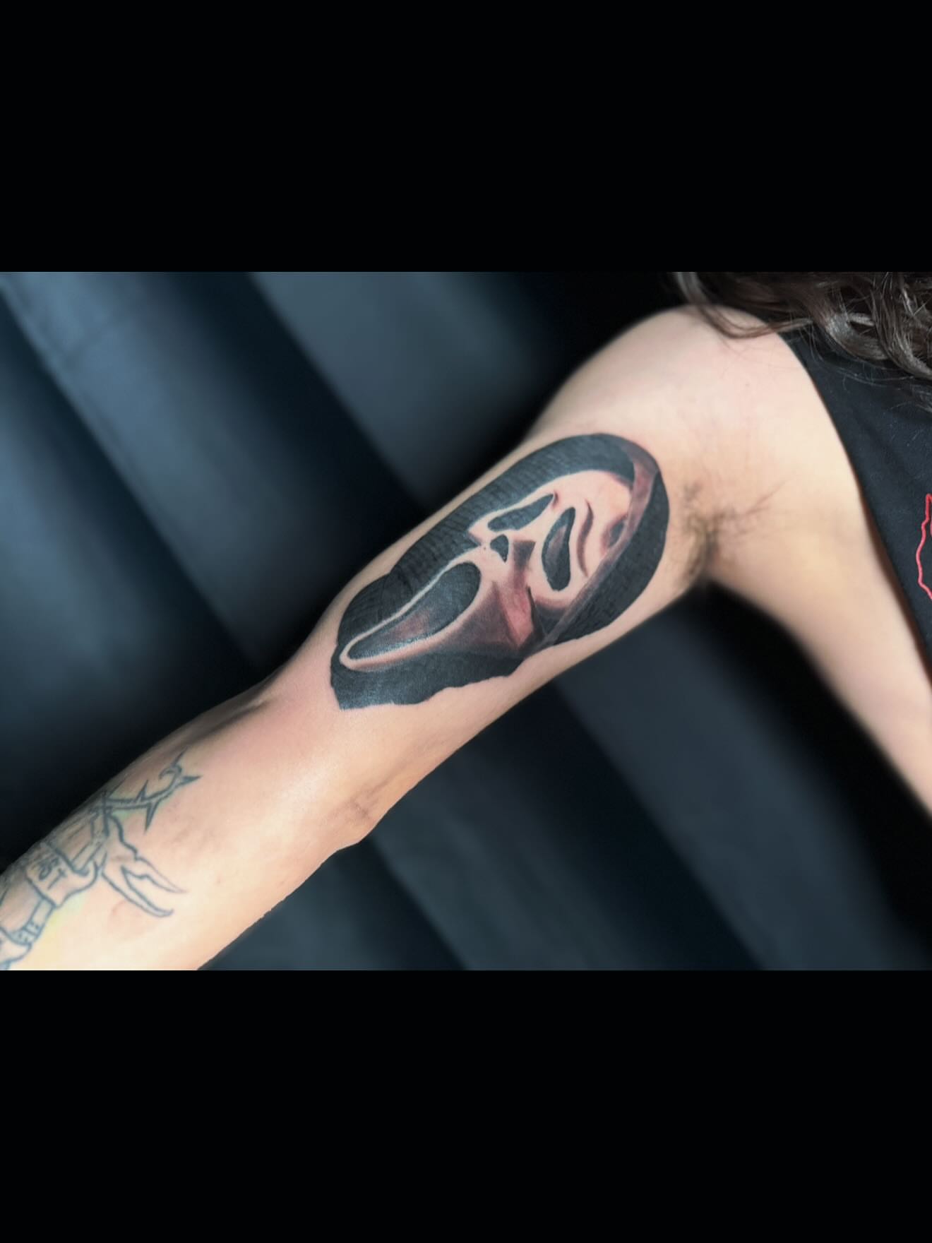Mask realism tattoo on the upper arm by Adrián Banuelos